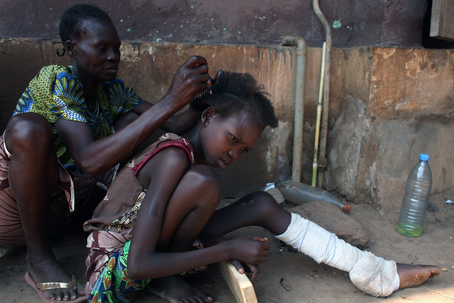 A woman, displaced as a result of religious violence, plaits the hair of her daughter who is nursing an injury at a hospital in Bossangao