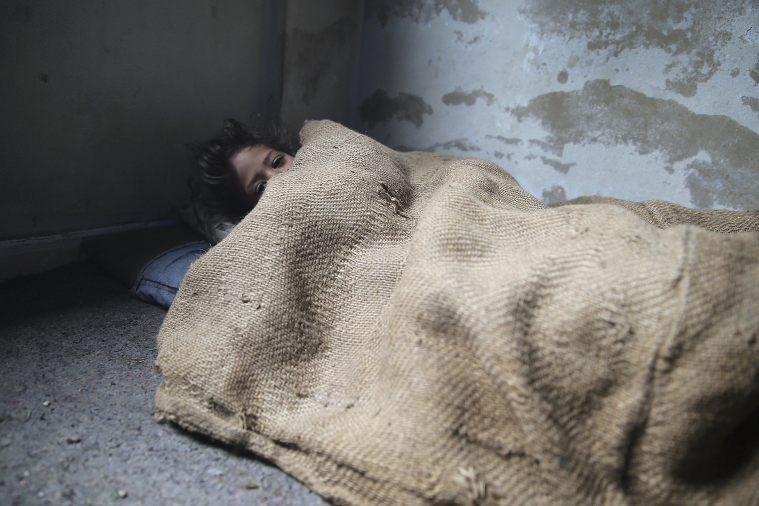 Girl covers herself with sackcloth due to a shortage in blankets in eastern Ghouta near Damascus