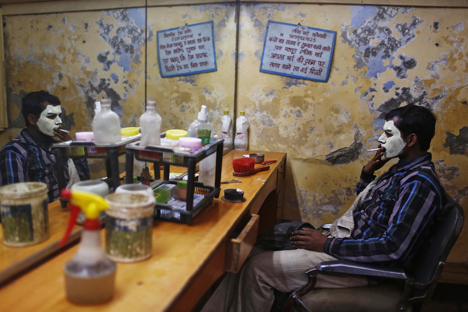 A migrant labourer with his face covered with facial cream, smokes as he waits for the cream to dry at a barber shop in New Delhi