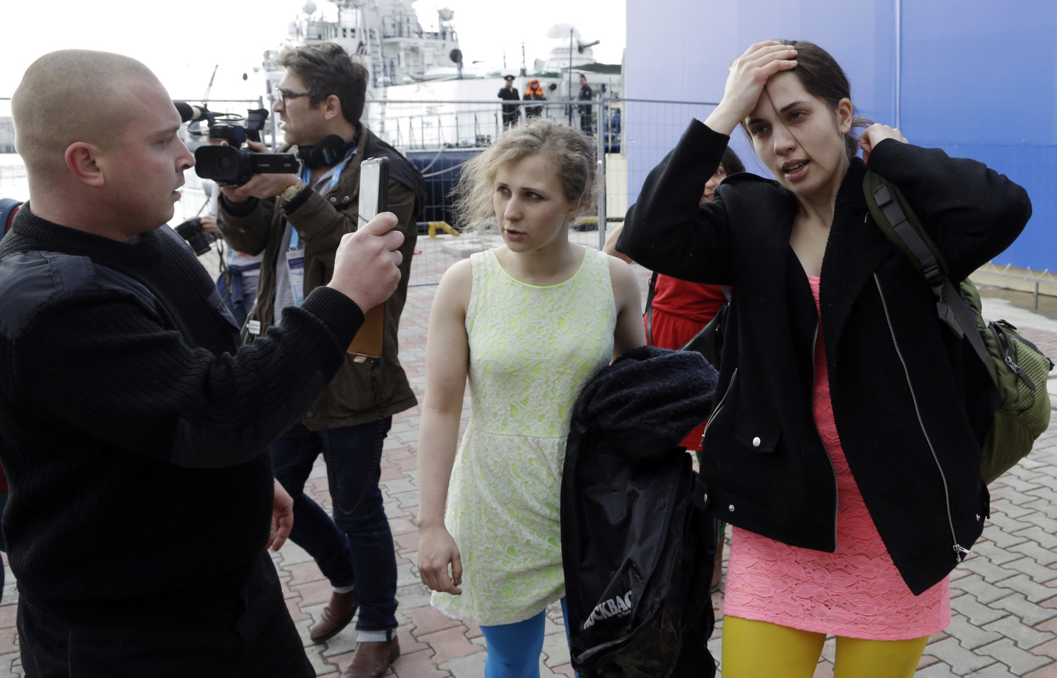 A Russian security officer records members of the punk group Pussy Riot Nadezhda Tolokonnikova, right, and Maria Alekhina, center, after they were attacked by Cossack militia in Sochi, Russia, on Wednesday, Feb. 19, 2014.