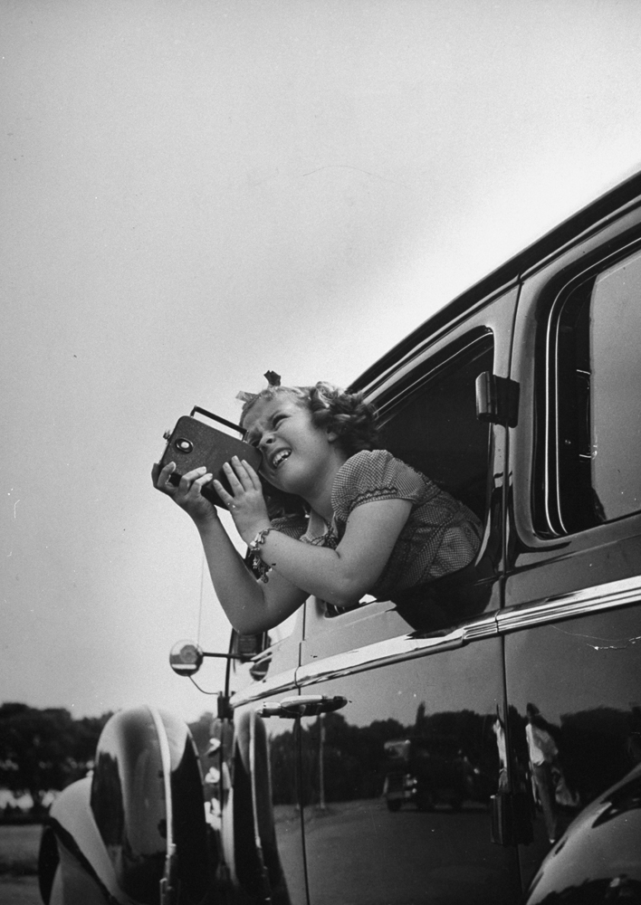 Shirley Temple taking pictures of famous sites in Washington, DC, from the window of a car, 1938.