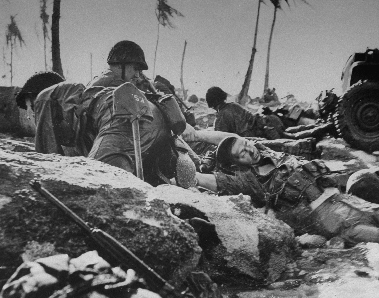 On the coral beach of Eniwetok's Engebi Island, a Marine drags a dead comrade out of the surf.
