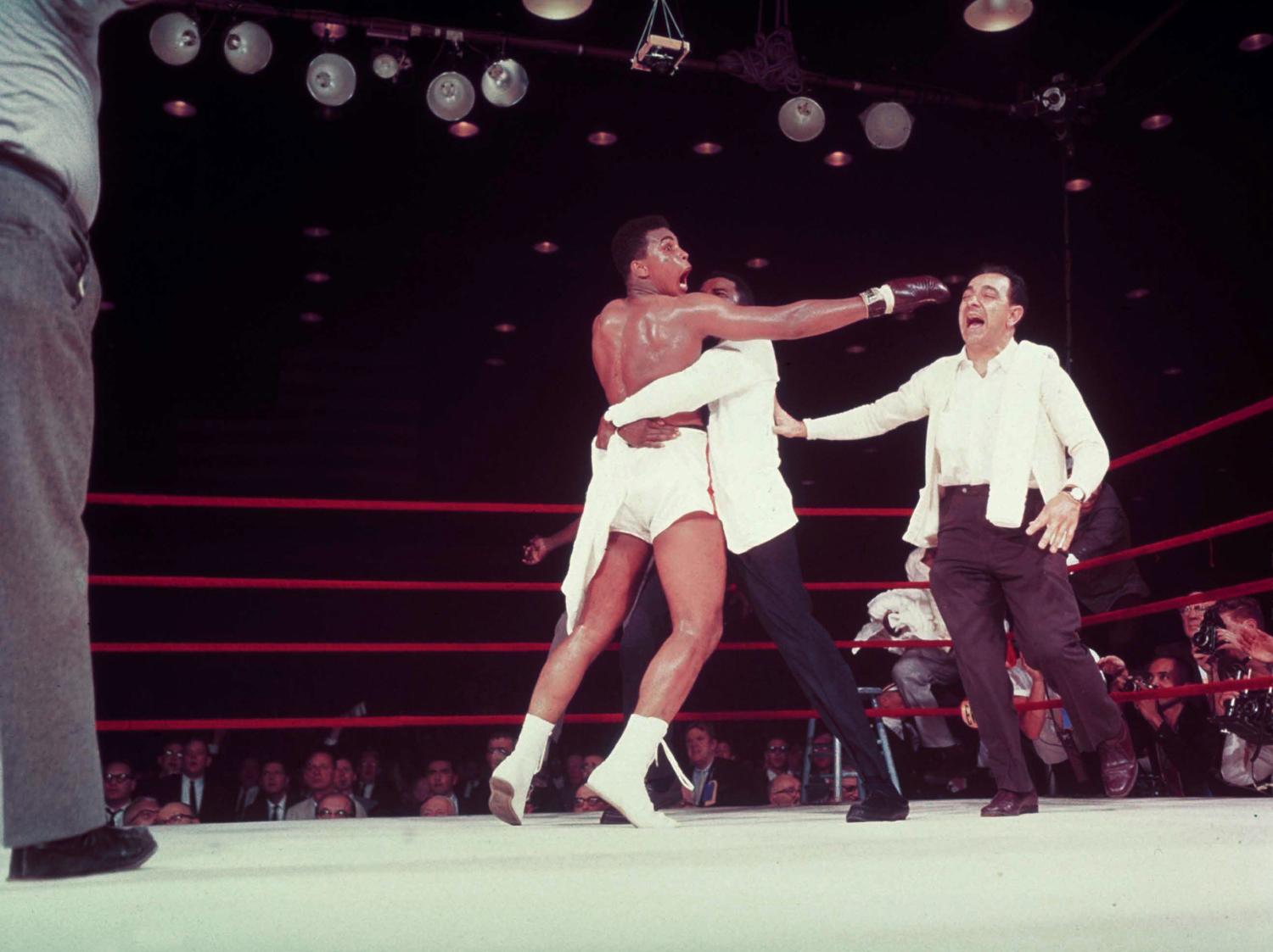 The fight is over. Clay shouts, 'I am so pretty!' as he realizes Liston won't come out for seventh round. Trainer Angelo Dundee rushes to Cassius as handler Bundini Brown tries to restrain the half-hysterical champ.