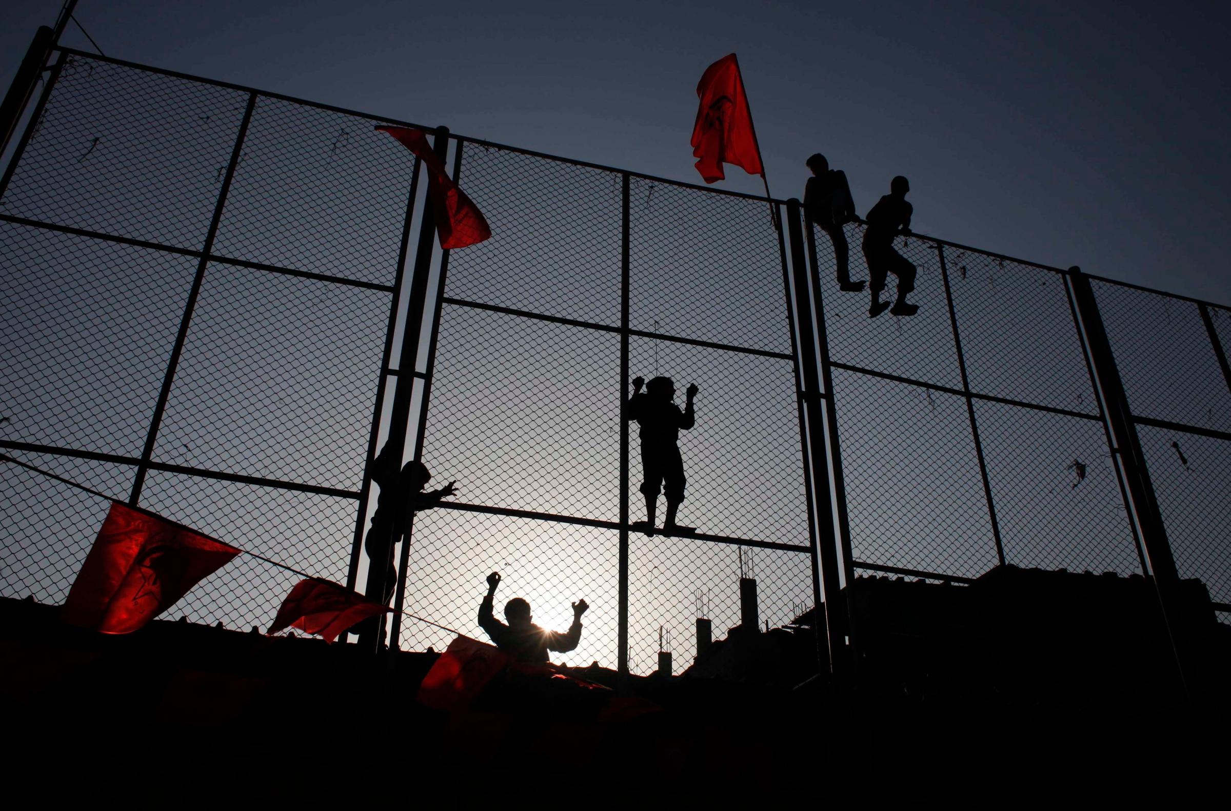 Palestinian boys climb a fence to watch a rally marking the 45th anniversary of the founding of the Democratic Front for the Liberation of Palestine (DFLP), in Rafah