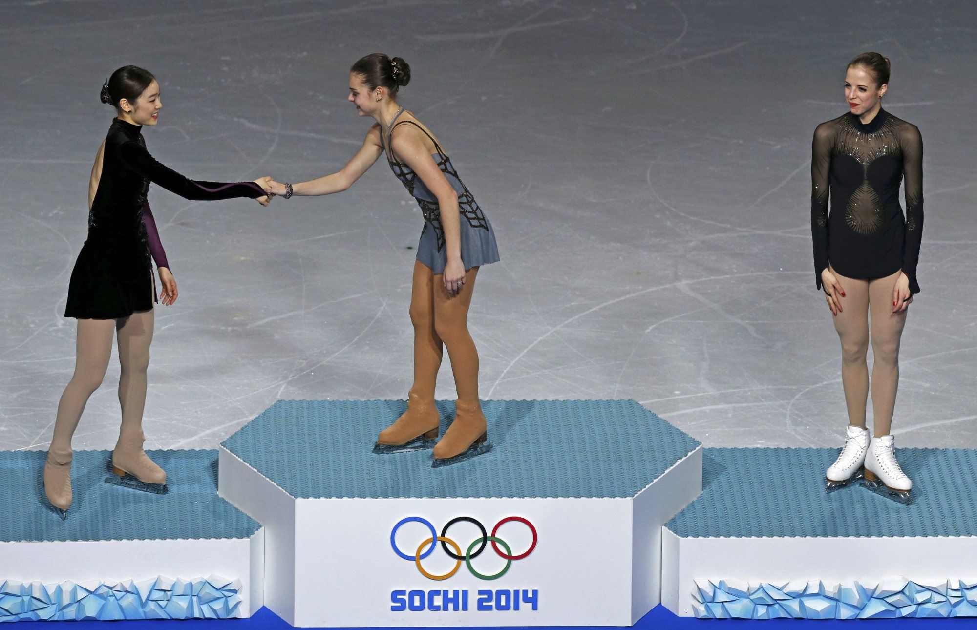 First-placed Russia's Adelina Sotnikova (C) shakes hands with second-placed South Korea's Kim Yuna (L) as third-placed Italy's Carolina Kostner looks on, on the podium after the figure skating women's free skating program.