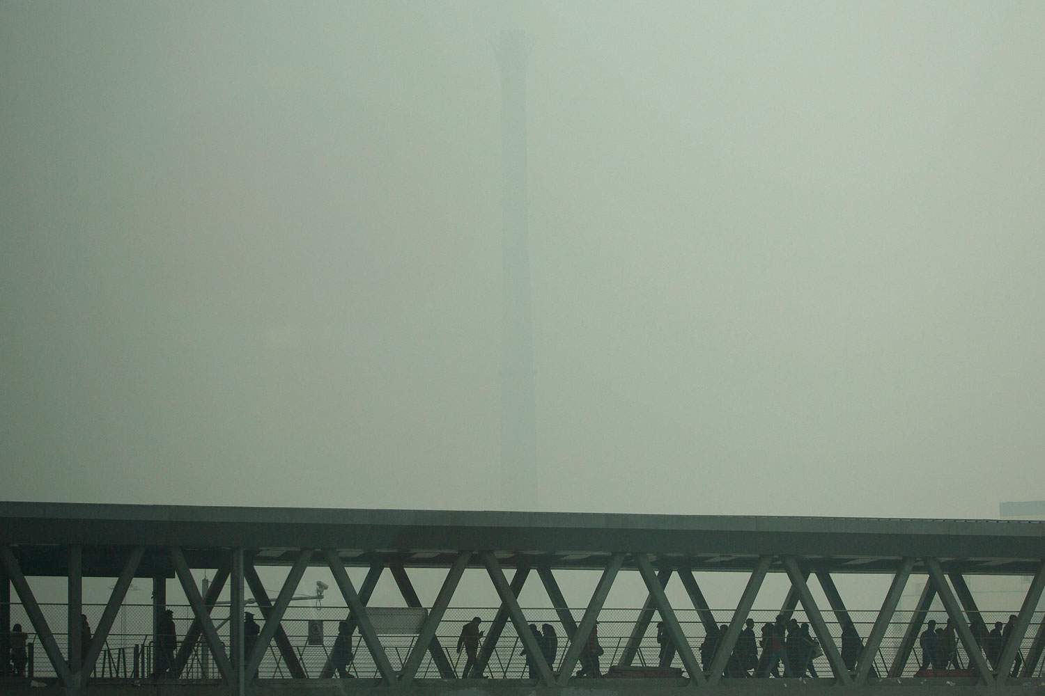 A chimney of a heating plant is obscured by heavy haze as commuters walk through a bridge linking a subway station and a bus station on a severely polluted day in Beijing, Feb. 25, 2014.