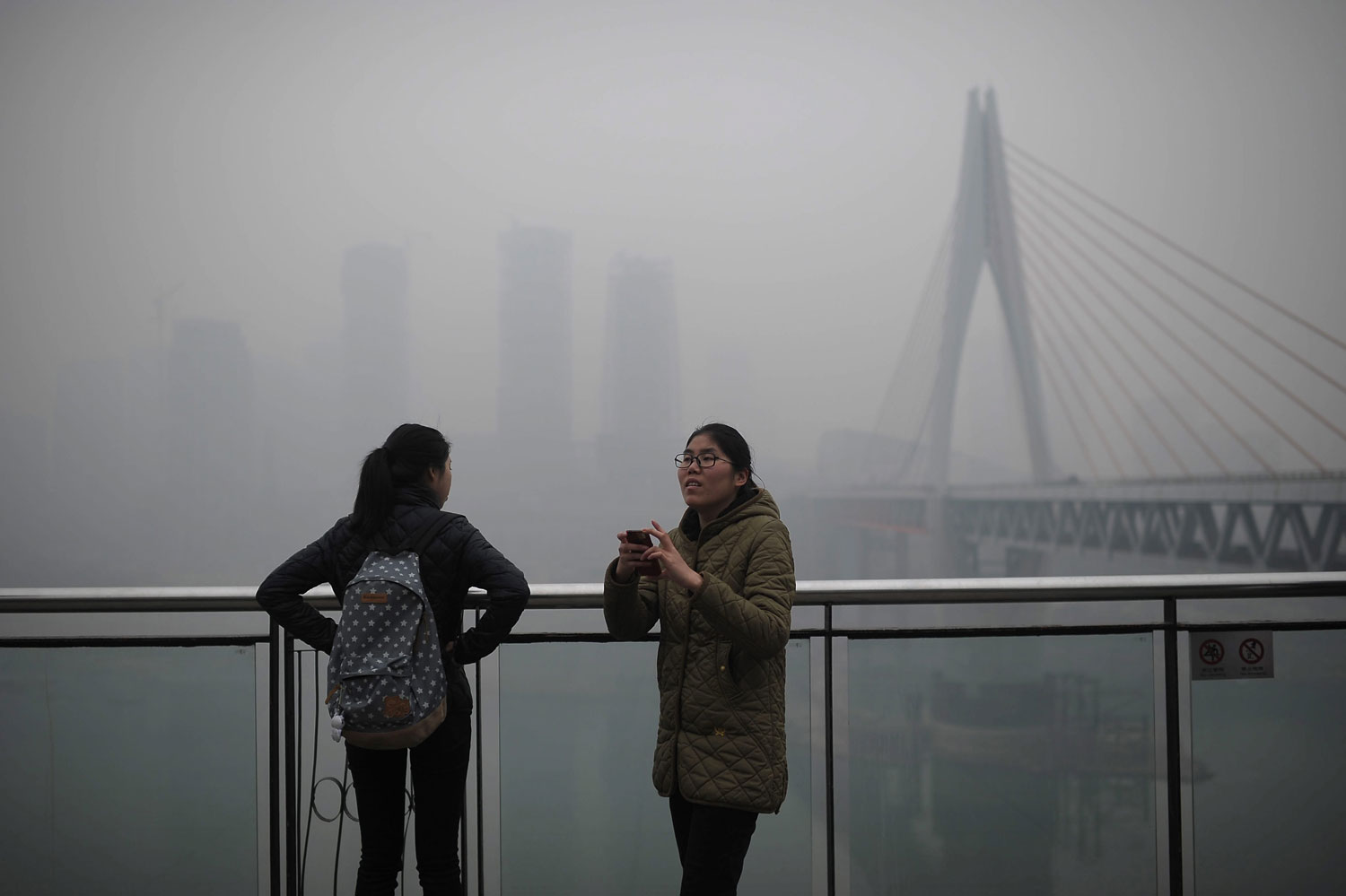 A woman tries to take photos on the river bank in the haze in southwest Chongqing Municipality, Feb. 23, 2014.