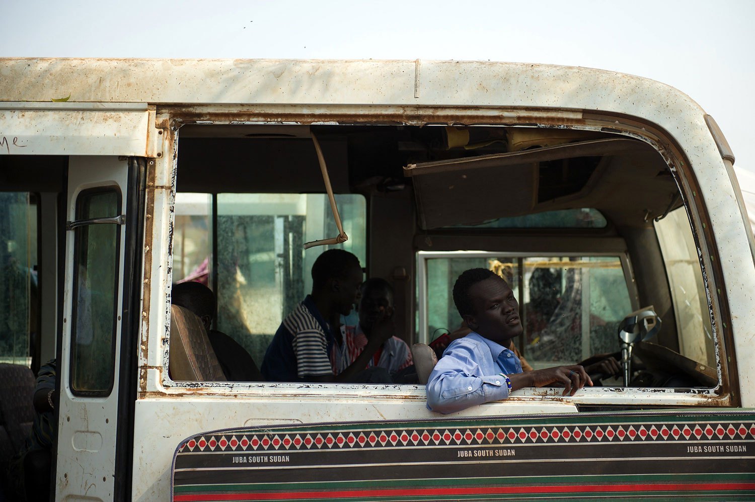 A South Sudanese man sits in the shell of an old bus in a spontaneous camp for internally displaced persons at the United Nations Mission to South Sudan base in Juba, South Sudan, on Jan. 9, 2014.