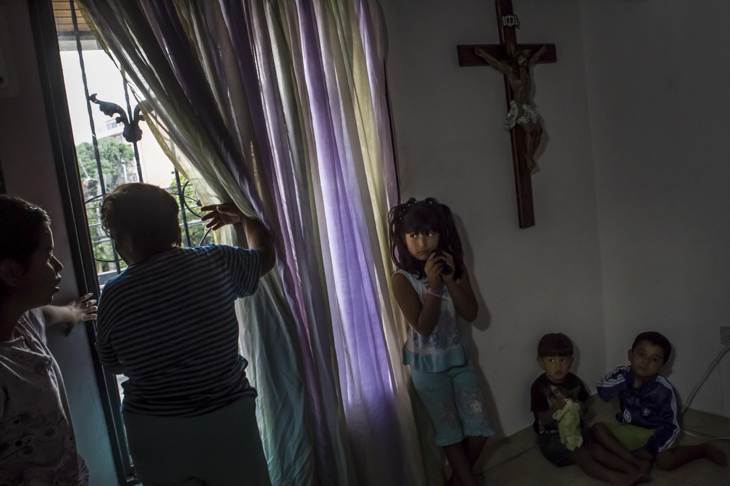 A family watch through a window as riot police and protesters clash in the street outside in San Cristobal.
