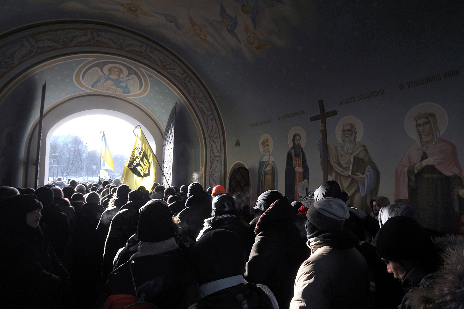 Ukrainian protesters hold their flags outside of Mikhaylovsky Cathedral as they pay their final respects to Belarussian protester Mikhail Zhiznevsky during a funeral service in Kiev on Jan. 26, 2014.