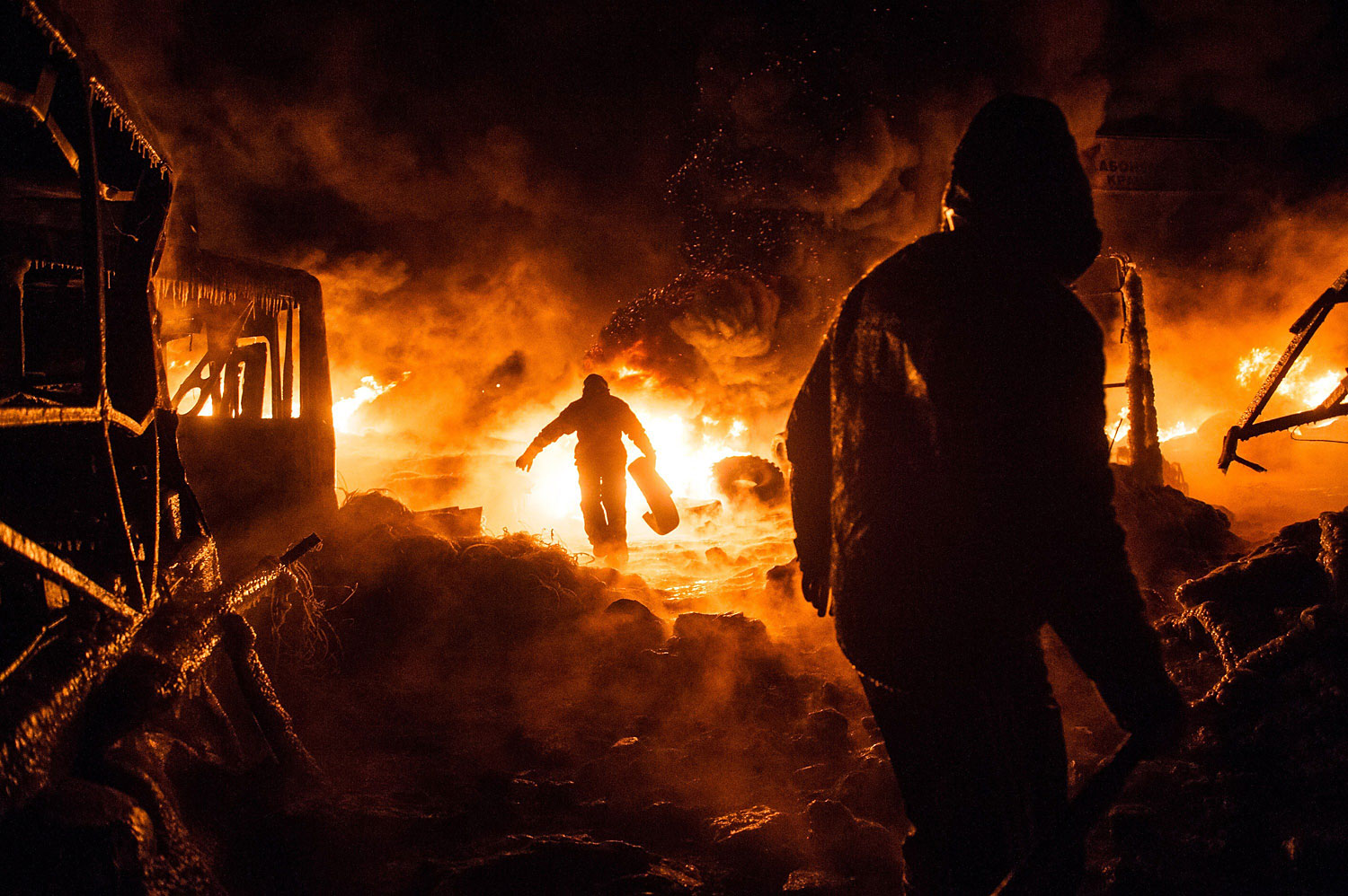 Ukrainian anti-government protesters walk past burning tyres during clashes with riot police in central Kiev early on Jan. 25, 2014.