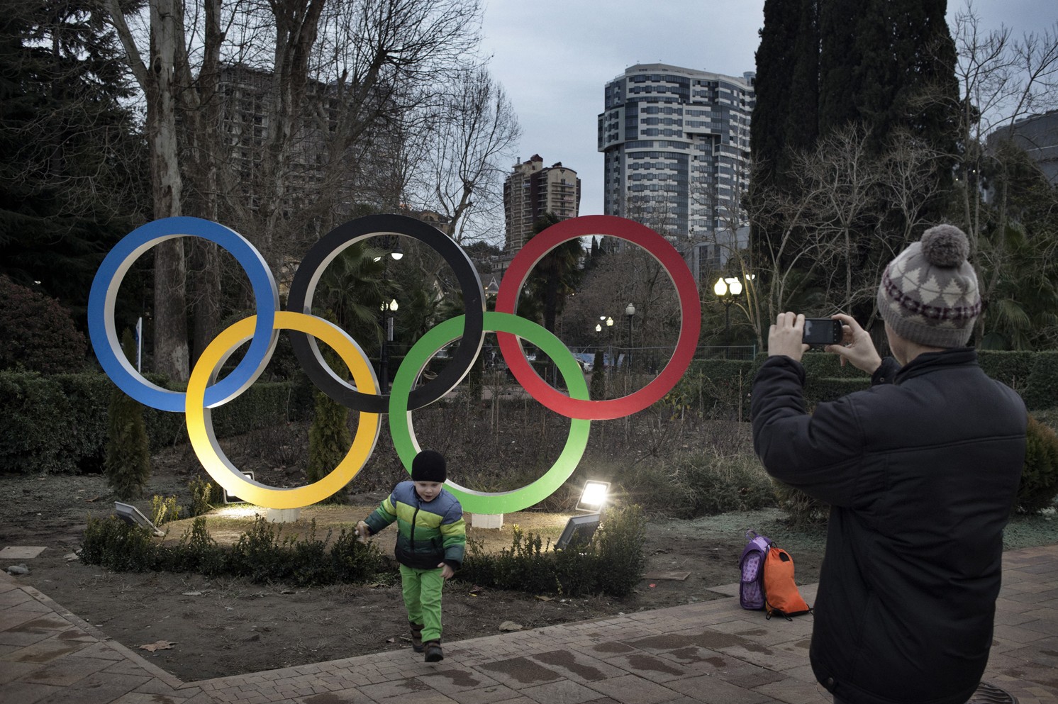 Sochi, Russia, January 2014: A man  takes photos of a boy in front of the Olympic  Rings.