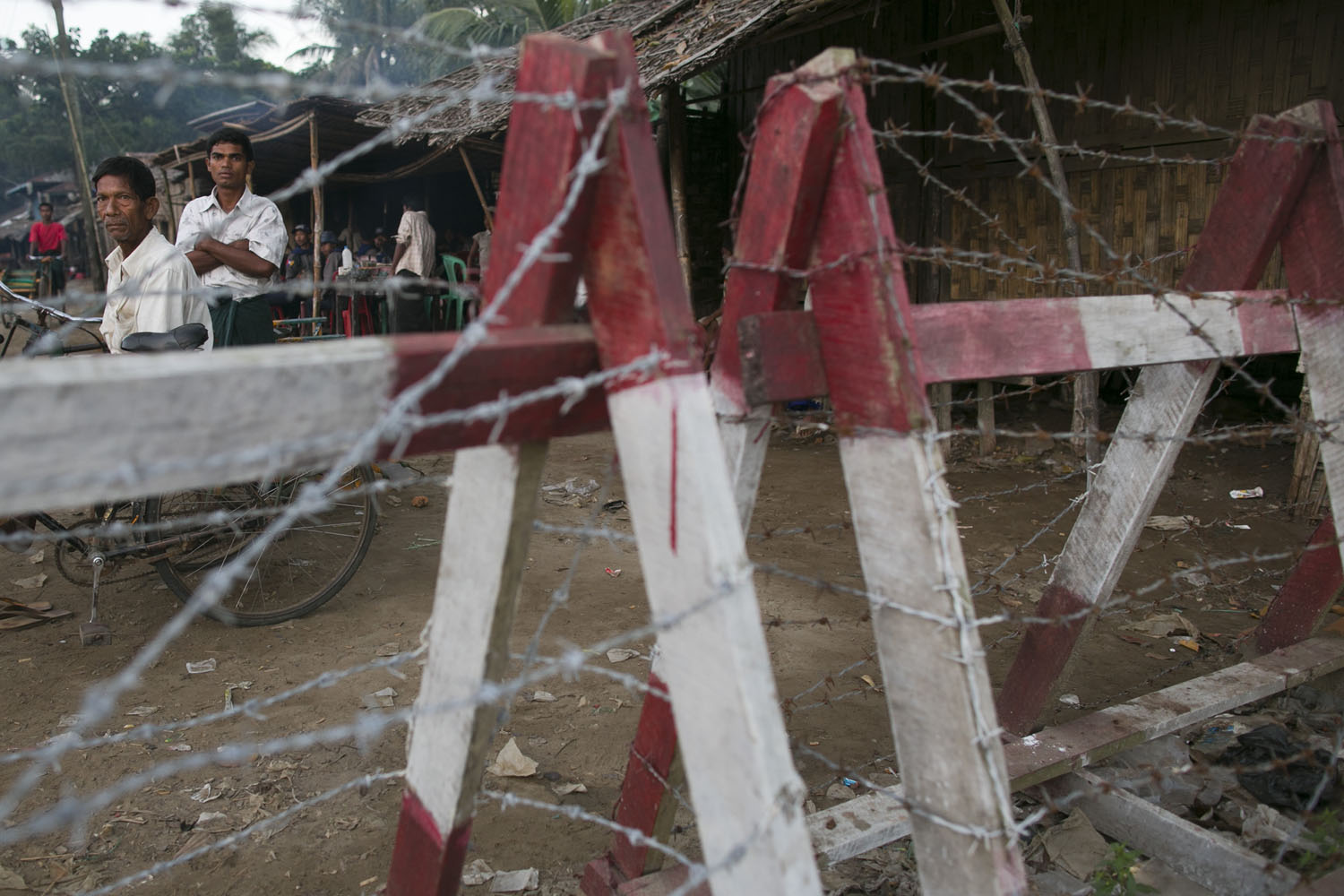 Rohingya men look out from behind a barbed-wire fence used as a barrier to restrict travel on Nov. 25, 2012, on the outskirts of Sittwe in Burma