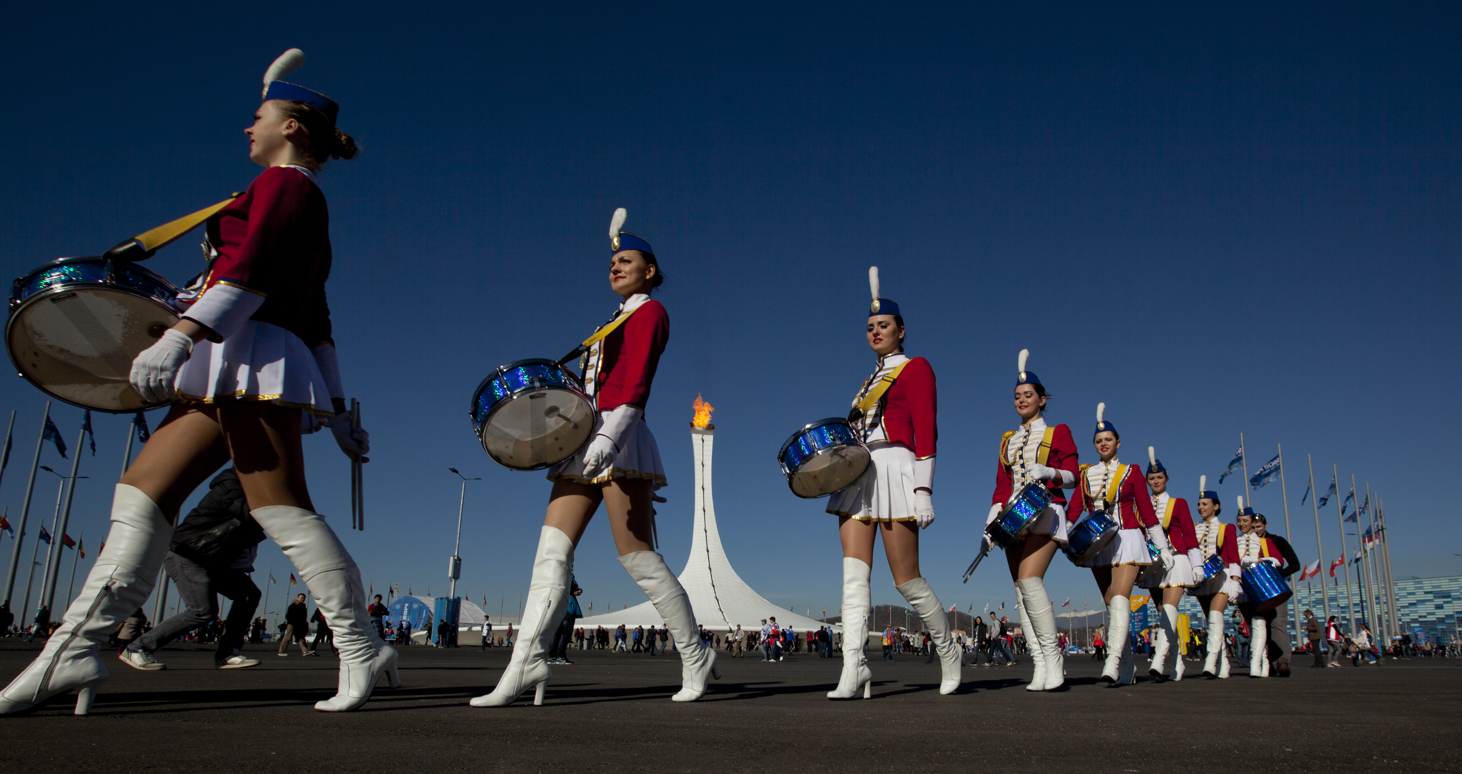 Cheerleaders walk to a venue past the burning Olympic cauldron during the 2014 Winter Olympics in Sochi, Russia, Feb. 13, 2014.
