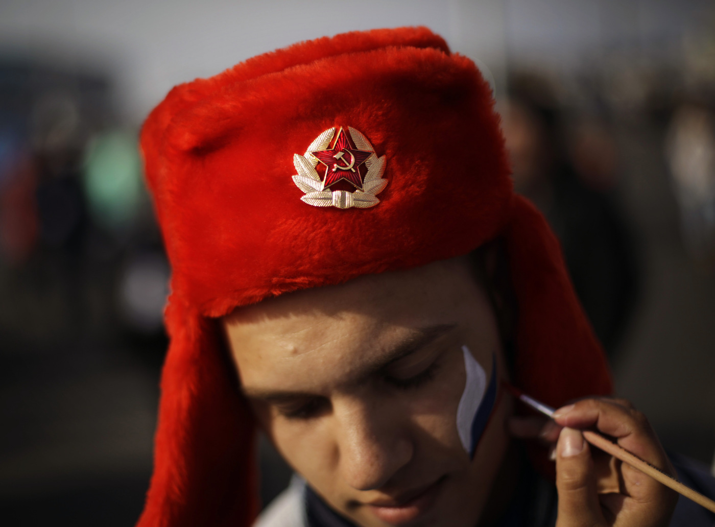 An emblem with the Soviet hammer and sickle decorates the hat of Serdar Yuldashev as he has his face painted in the colors of the Russian flag.