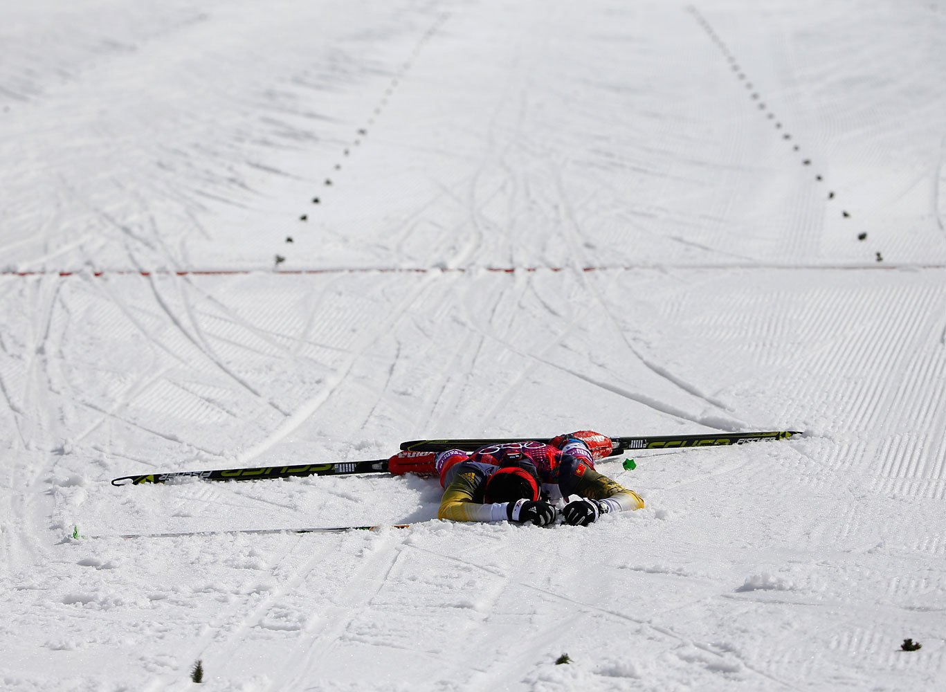 China's Xu Wenlong lies on the ground after crossing the finish line in last place in the men's cross-country 50 km mass start free.