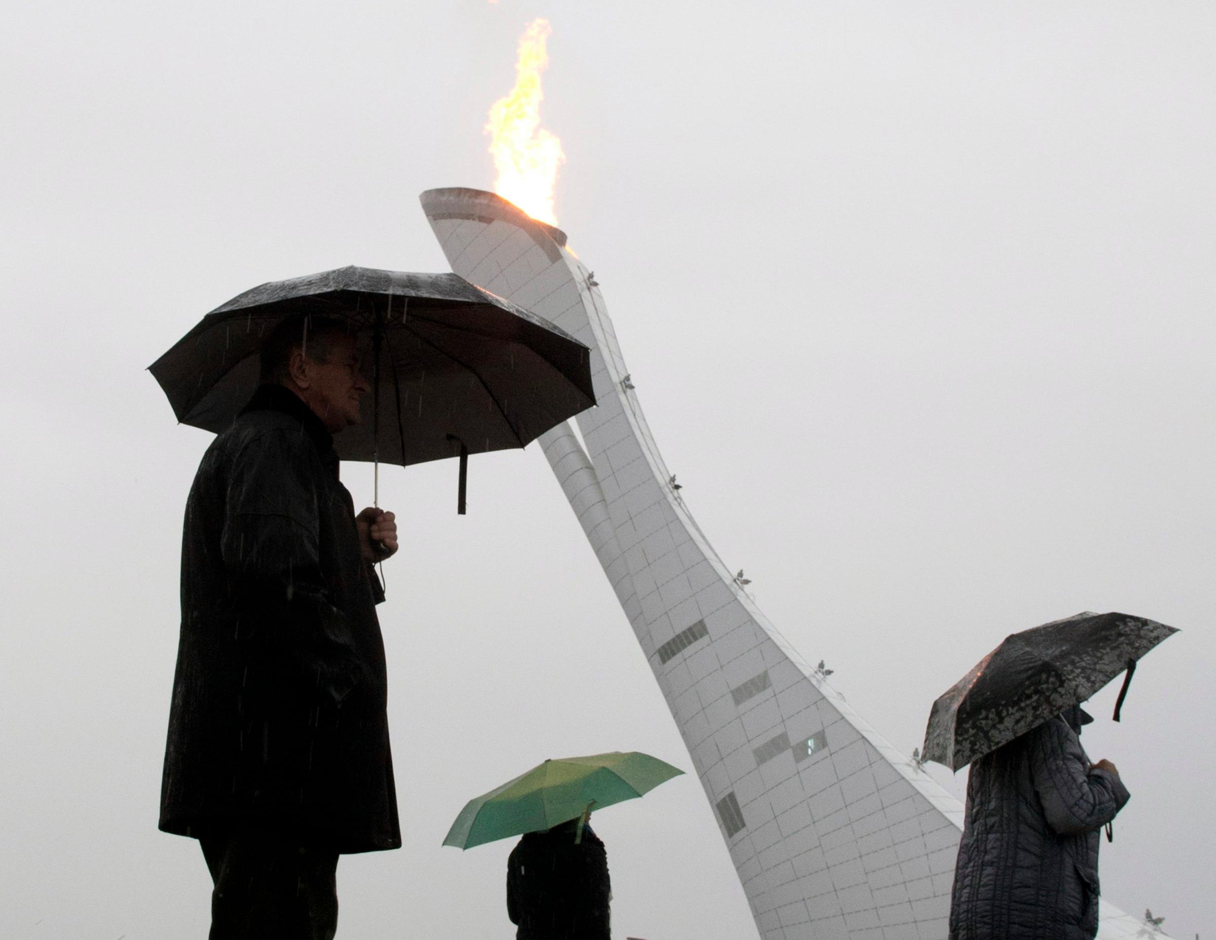 Visitors to the Olympic park walk past the Olympic cauldron as it rains at the Sochi Winter Olympics.