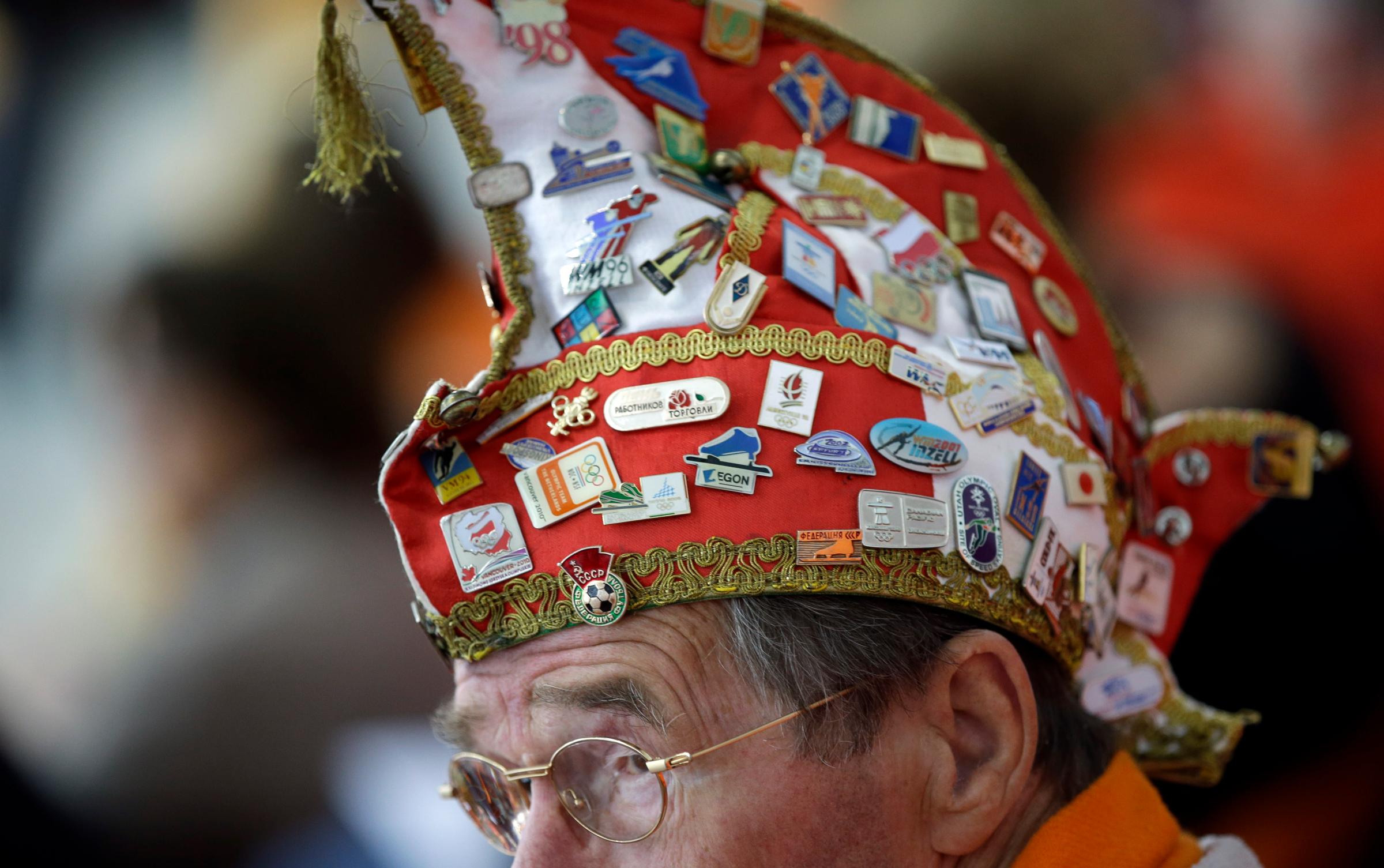 A Dutch skating fan, his hat filled with Olympic pins, watches the women's 1,000-meter speedskating race during the 2014 Winter Olympics in Sochi, Russia, Feb. 13, 2014.