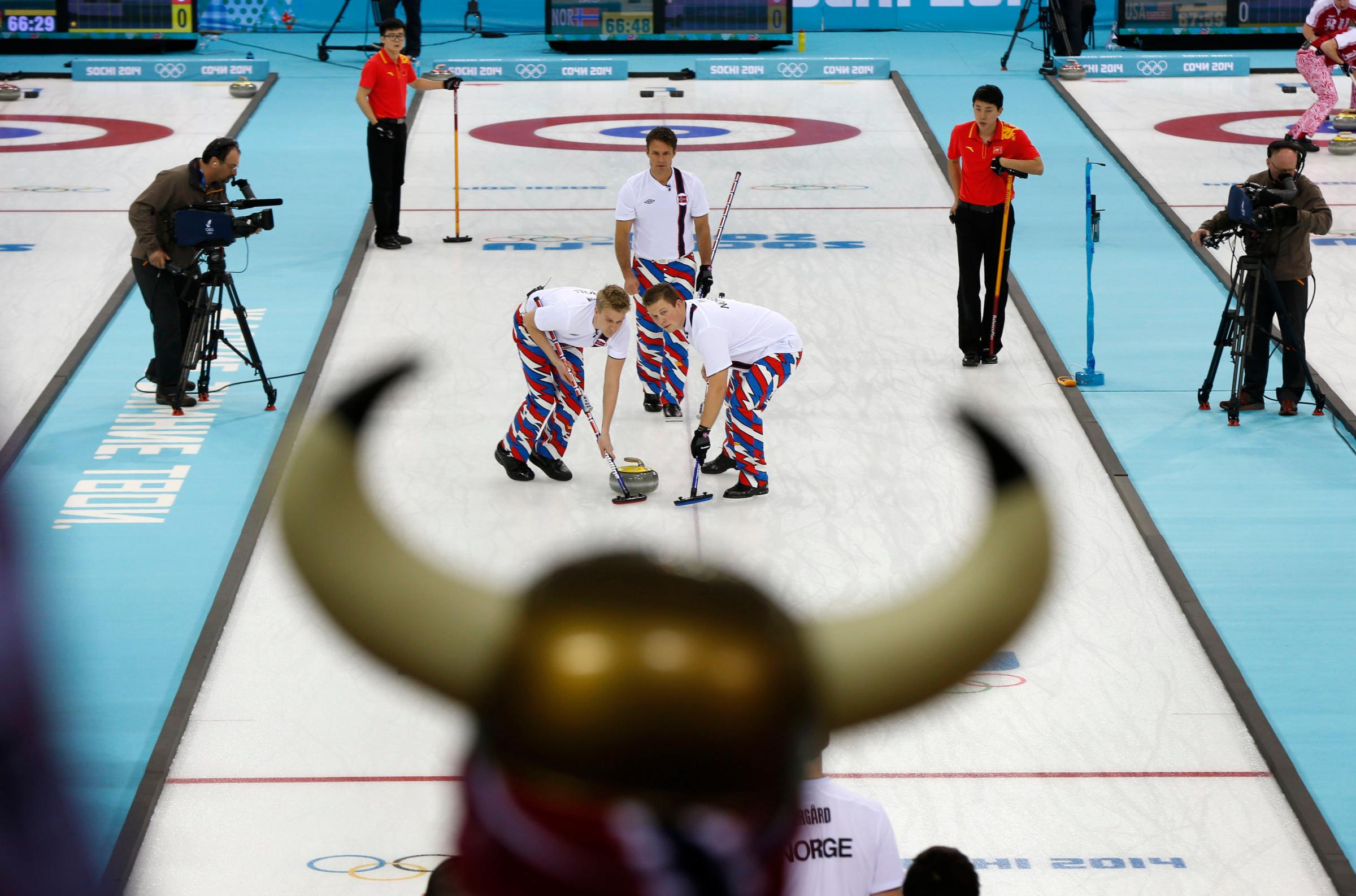 Norwegian curling fan Rune Eikeland, wearing viking horns, watches his countrymen Haavard Vad Petersson, left, and Christoffer Svae sweep in front of a rock delivered by skip Thomas Ulsrud during the men's curling competition against China.