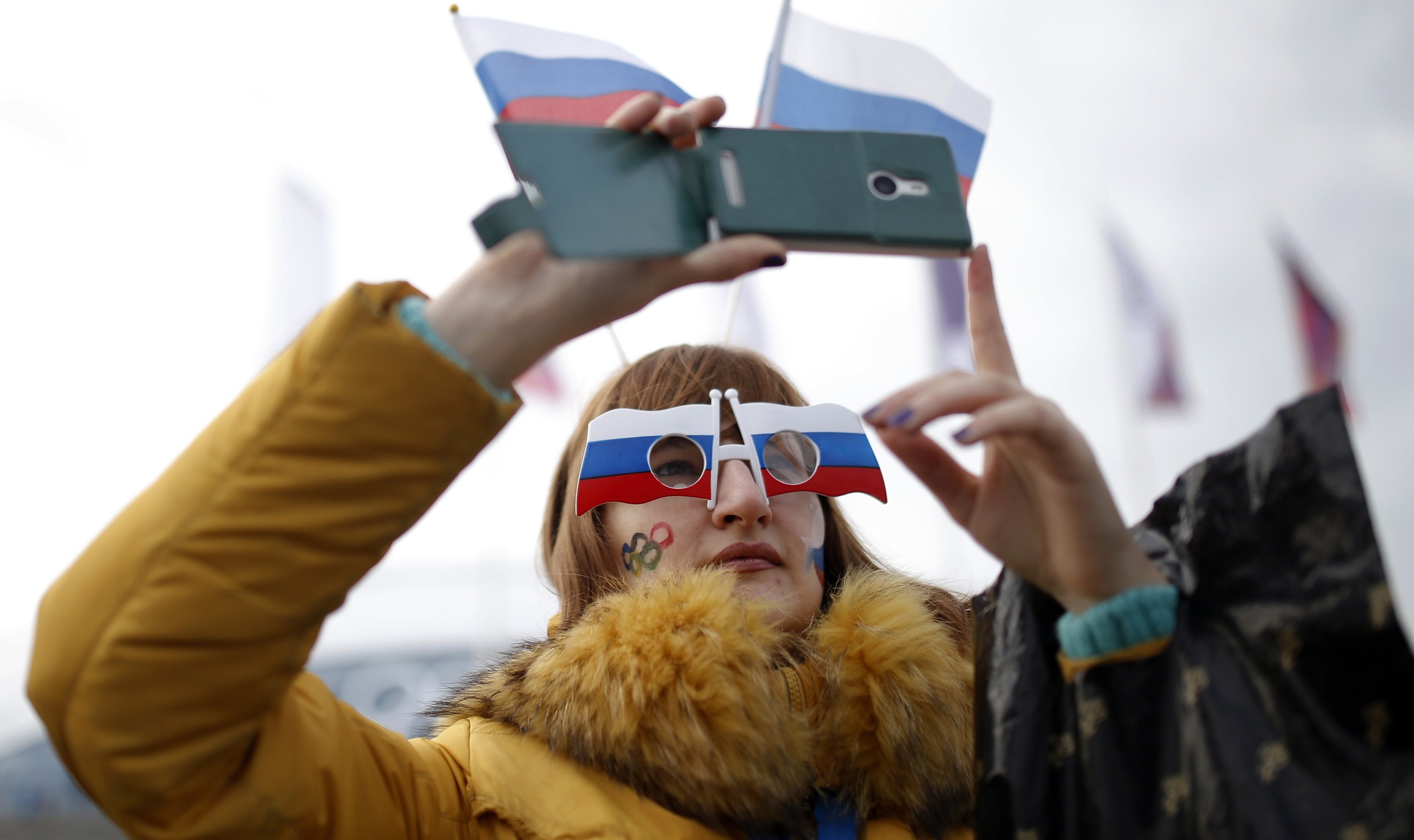 A woman sports the Russian national flag with her eyewear and takes photographs with a smart phone at Olympic Park.