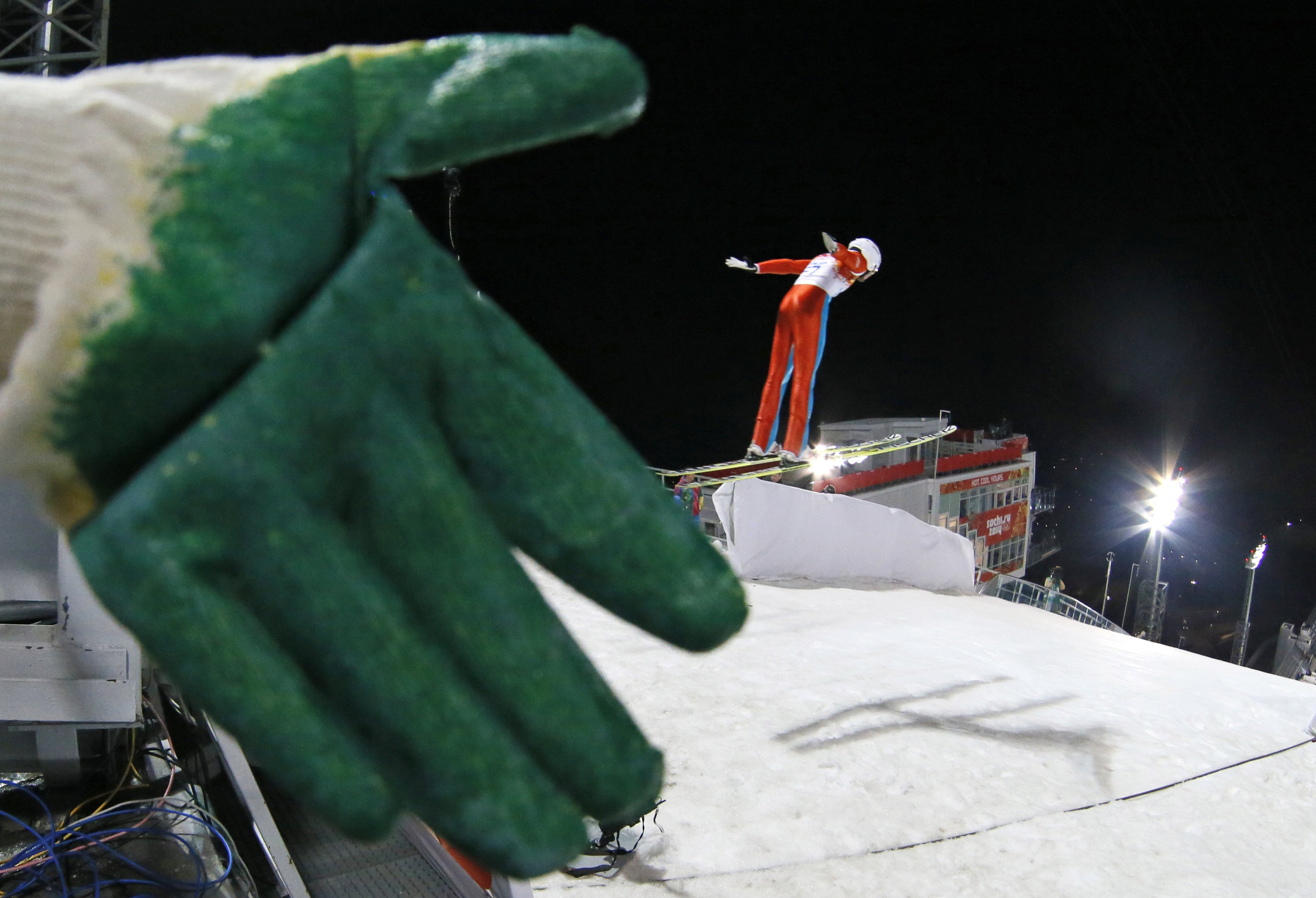 A fore jumper passes by a working glove left behind on the railing of the hill during a women's normal hill ski jumping training at the 2014 Winter Olympics, Monday, Feb. 10, 2014, in Krasnaya Polyana, Russia.