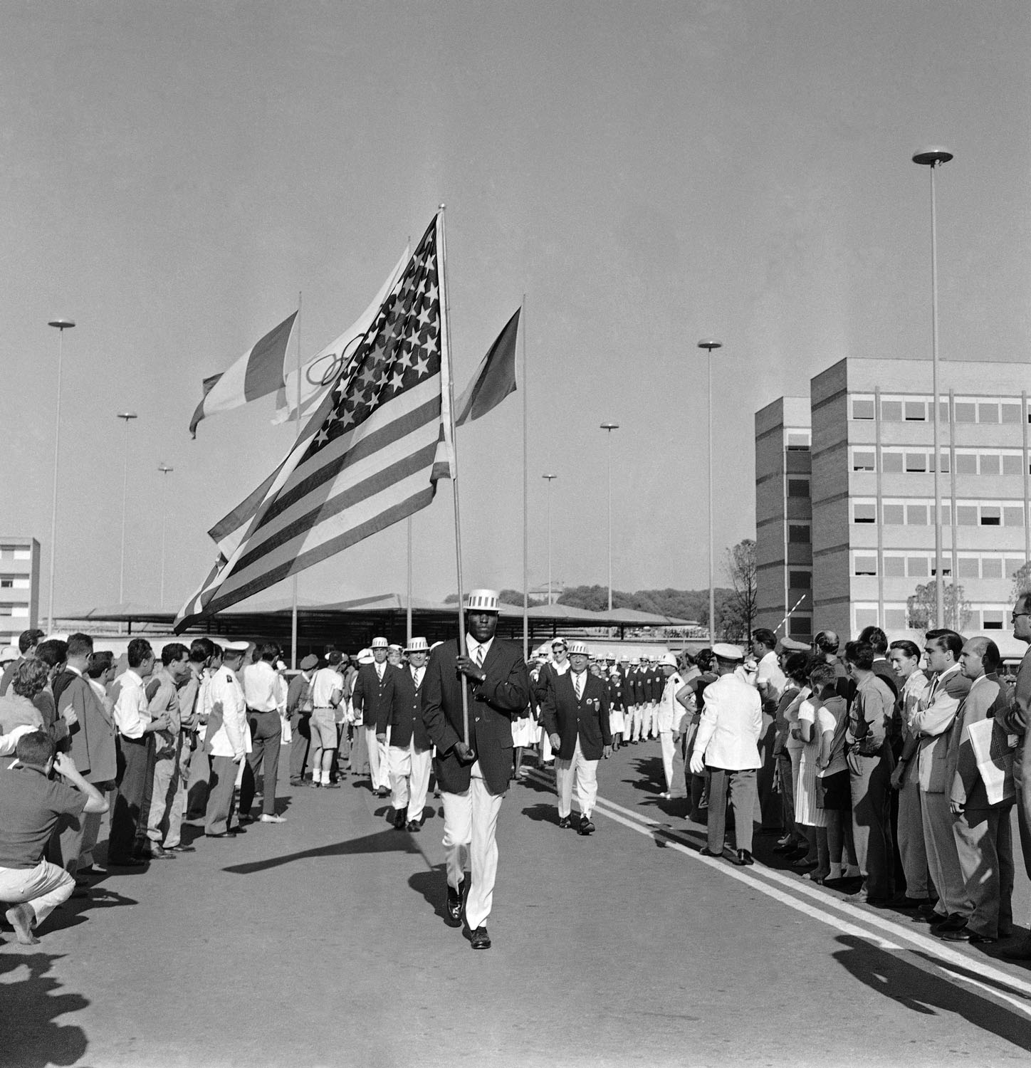 Track and Field athlete Rafer Johnson carries the American flag while leading his team out of the Olympic Village to march in the opening ceremony of the Rome Summer Olympics in 1960.