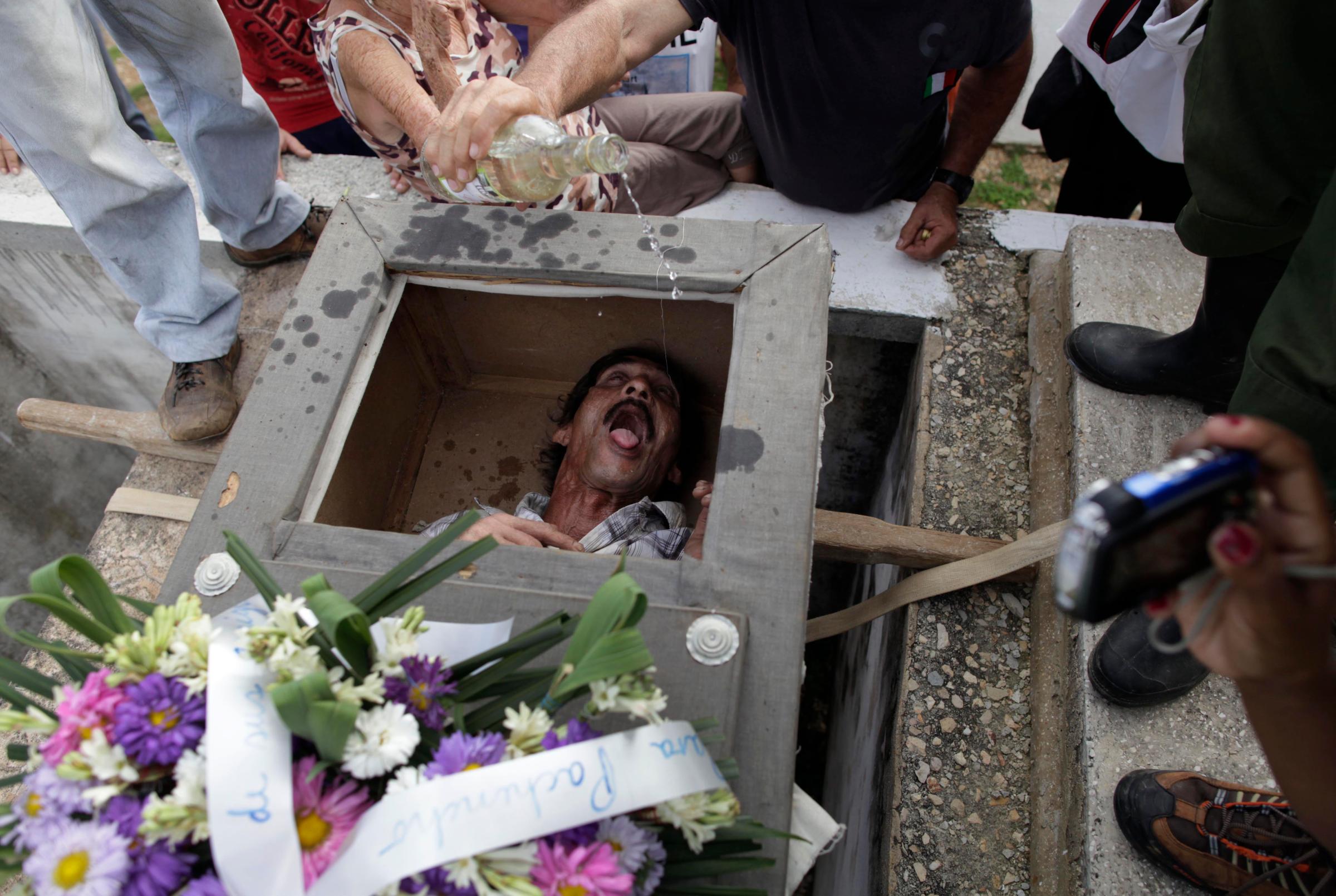 Divaldo Aguiar, who plays the part of Pachencho, lies inside a mock coffin as villagers splash rum into Aguiar's mouth during the Burial of Pachencho celebration at a cemetery in Santiago de Las Vegas, Cuba, Feb. 5.