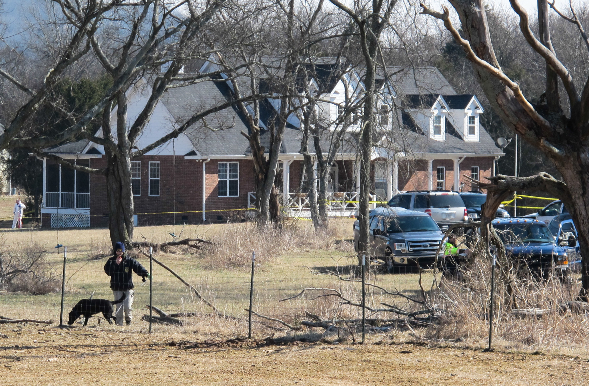 An officer and a dog inspect a fence near a home in Lebanon, Tenn., on Tuesday, Feb. 11, 2014, where police said a package exploded, killing a 74-year-old man and his wife.