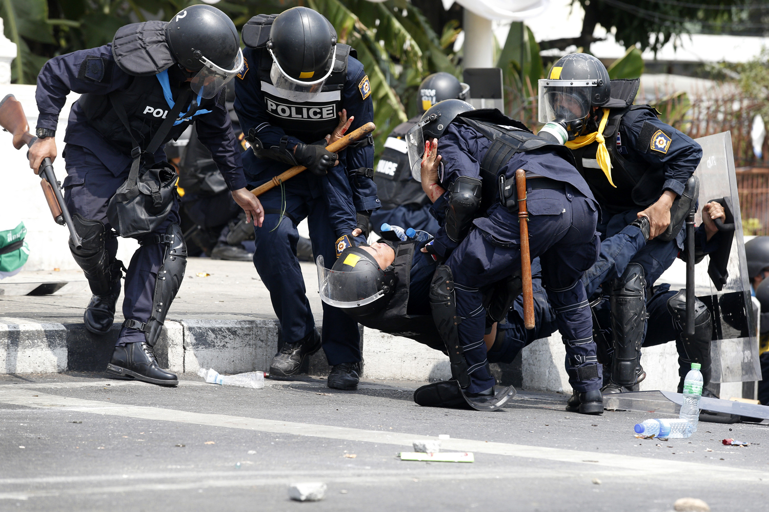 Thai police officers assist a colleague after an explosion during clashes with anti-government protesters near Government House in Bangkok