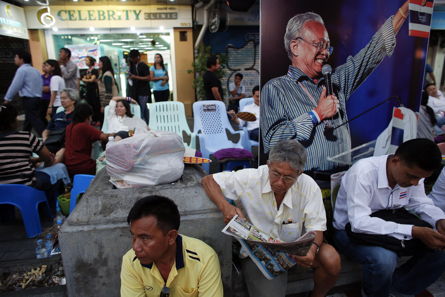 Anti-government protesters enjoy a massage and read papers near a picture of protest leader Suthep Thaugsuban in an occupied area, in downtown Bangkok