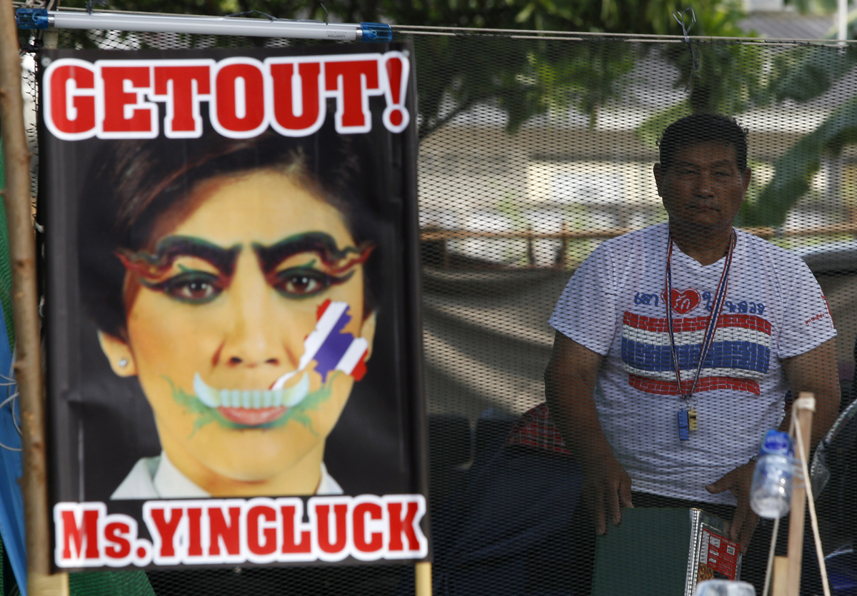 An anti-government protester stands next to a defaced image of Thailand's PM Yingluck during a rally in Bangkok