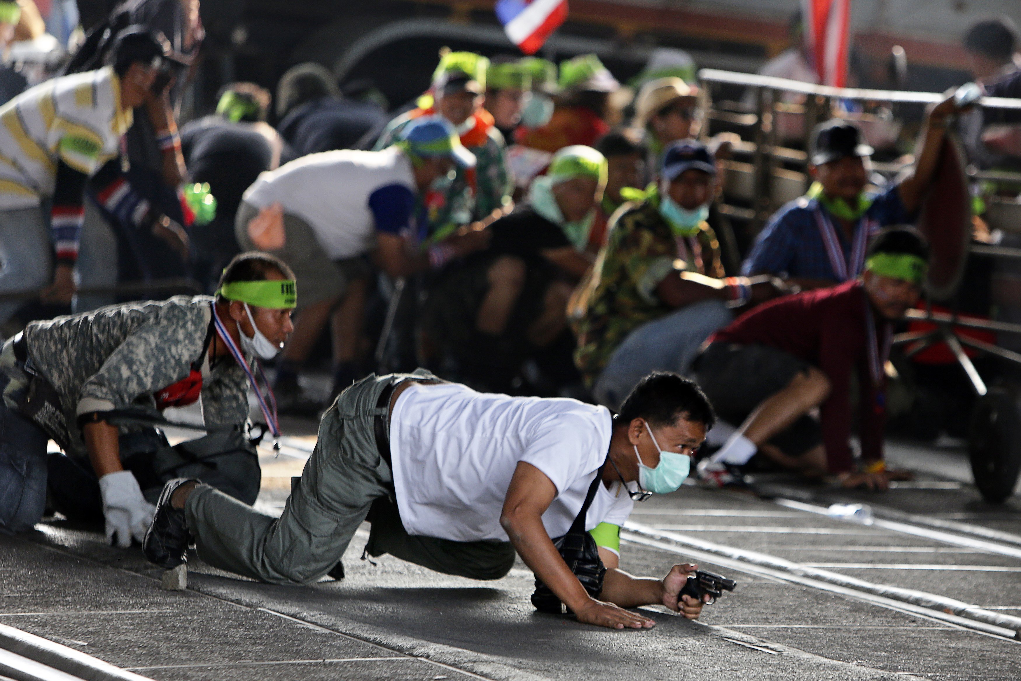 An anti-government protester crowls with his pistol during a gunfight between supporters and opponents of Thailand's government near Laksi district office in Bangkok