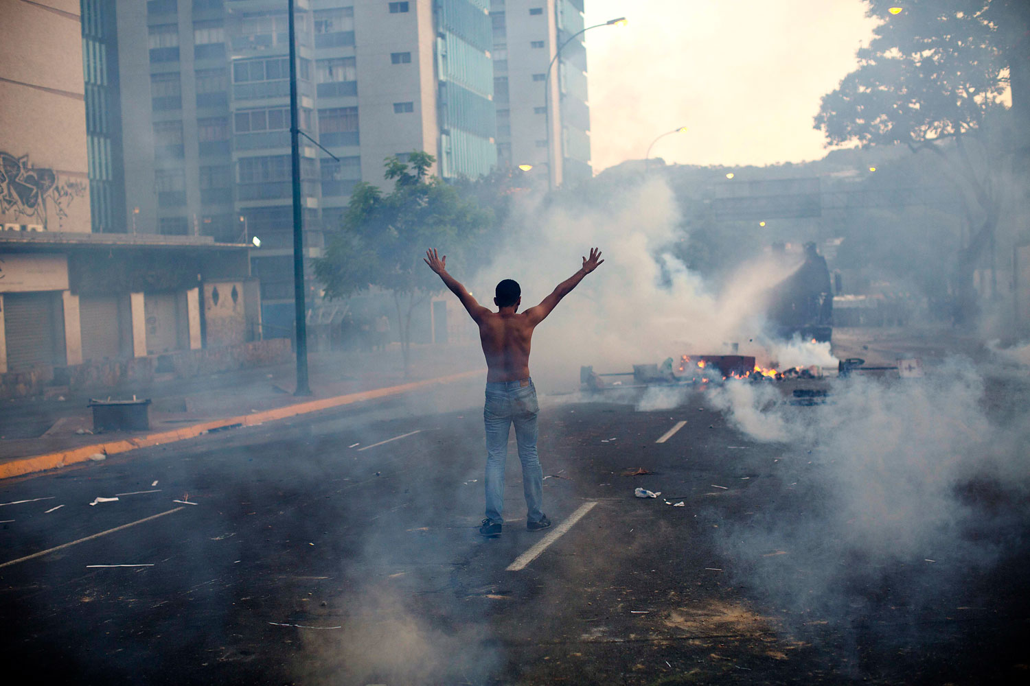 A demonstrator raises his arms toward the Bolivarian National Police firing tear gas and a water canon in the Altamira neighborhood of Caracas, Feb. 19, 2014.