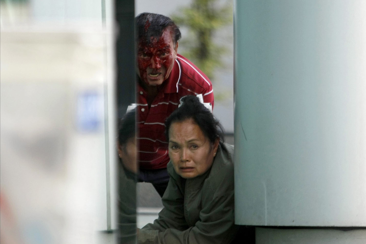 Feb. 1, 2014. A injured Thai man and a woman peer around a wall during a gun battle between anti-government protesters with government supporters near Lak Si district office in Bangkok.
