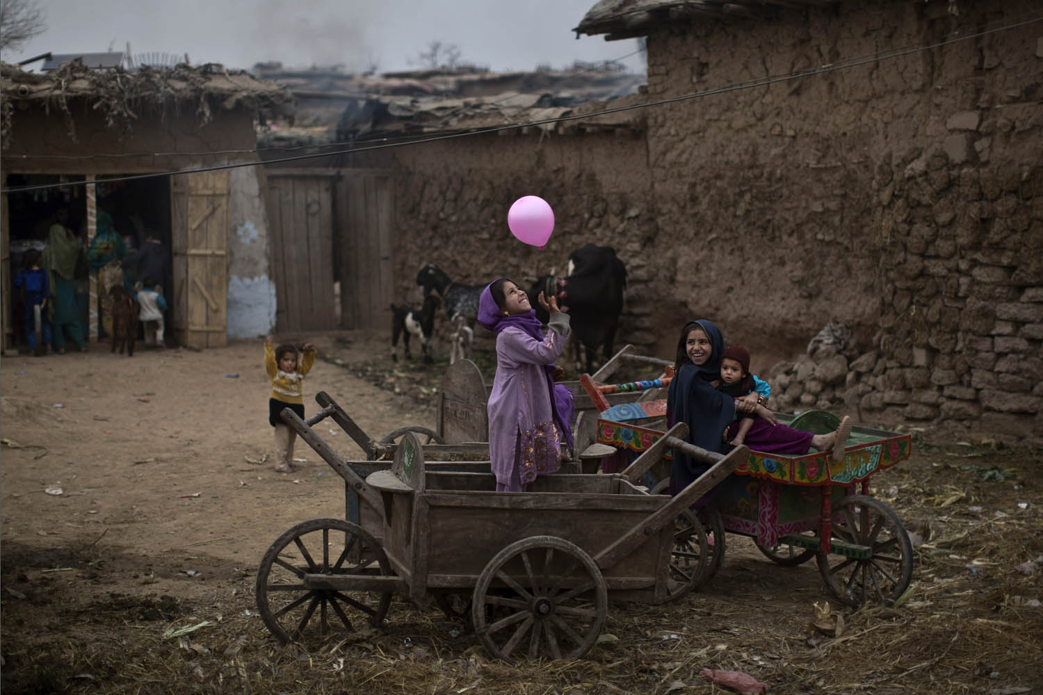 Feb. 2, 2014. An Afghan refugee girl, right, holding her younger brother, sits on a wooden-cart looking at her friend playing with a balloon in a poor neighborhood on the outskirts of Islamabad.