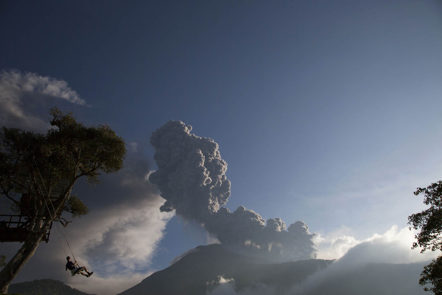 Boy plays on a swing as the Tungurahua volcano erupts in Banos