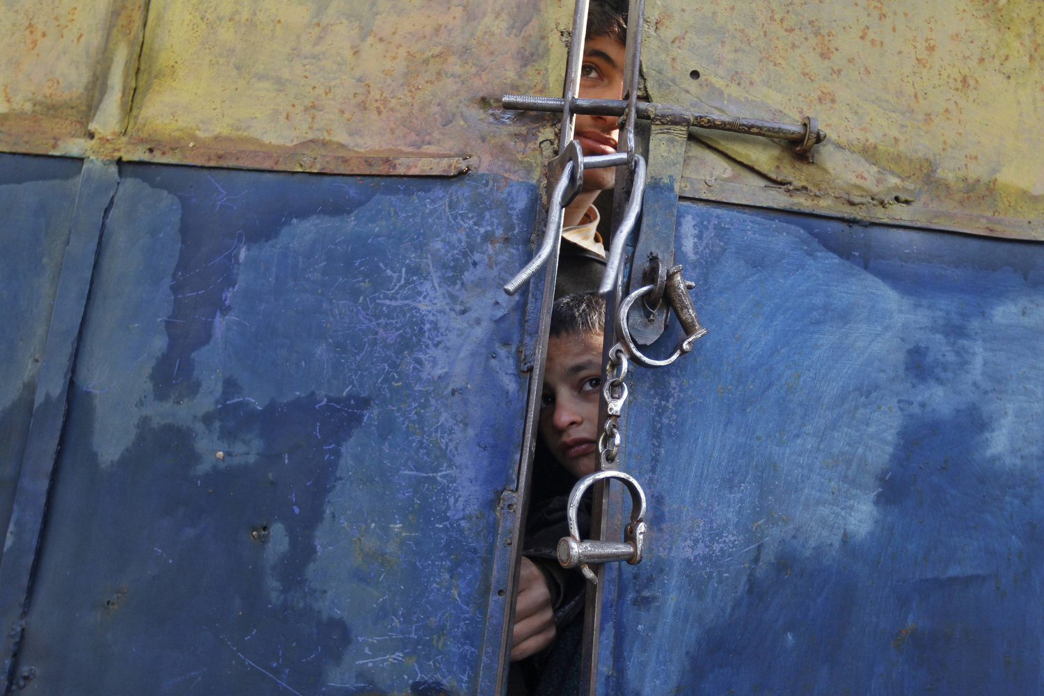 Boys peer through the gate of a police station to look at bodies of suspected militants in Lalpora