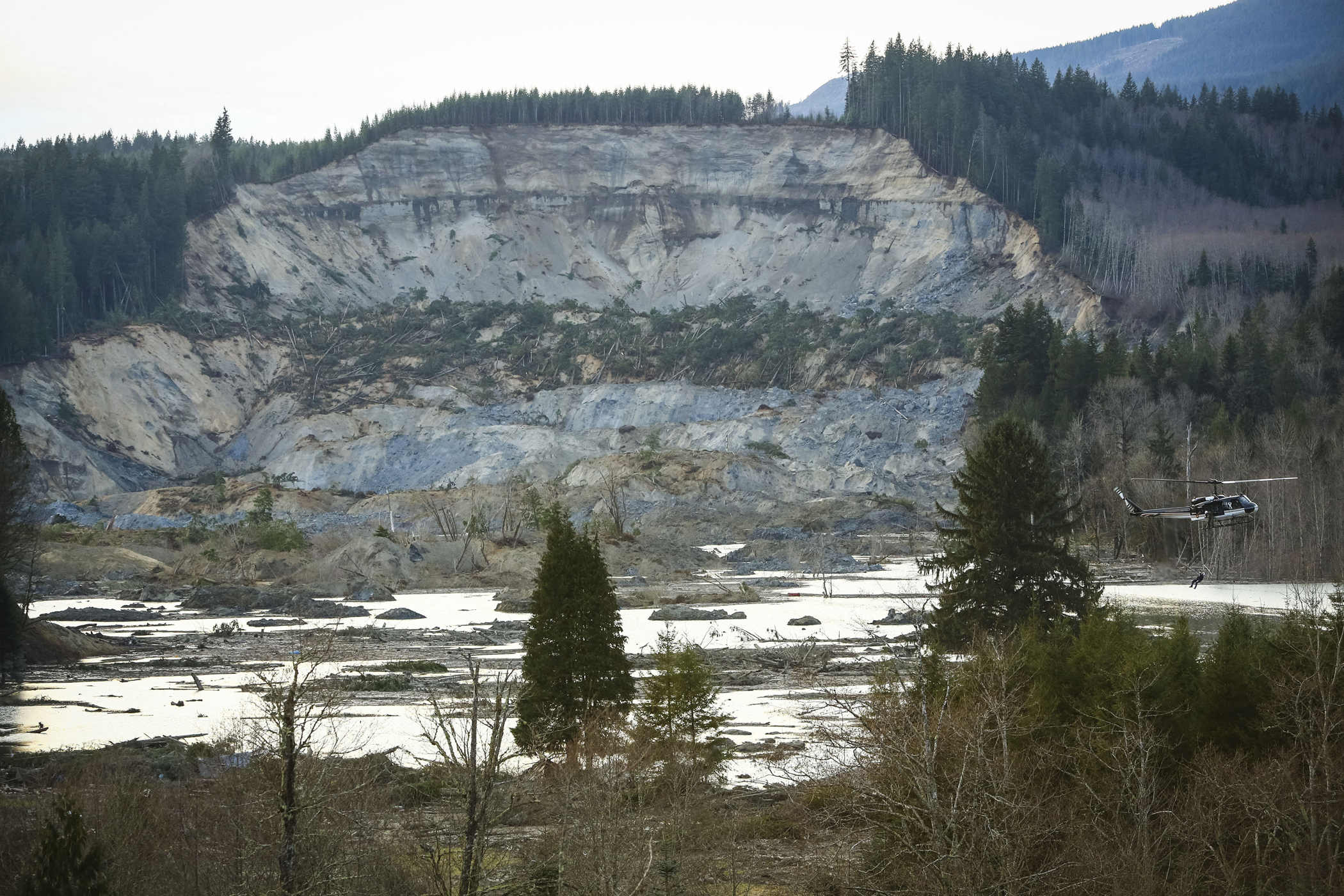 A rescue worker is lowered from a helicopter, right, near Oso, Wash, Monday, March 24, 2014.