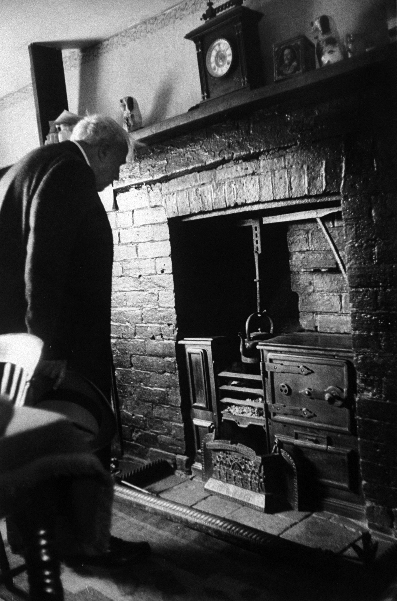 Frost, who once wrote, 'I never heard of a house that throve . . . where the chimney started above the stove,' examines stove of his old kitchen at Little Iddens, Gloucestershire