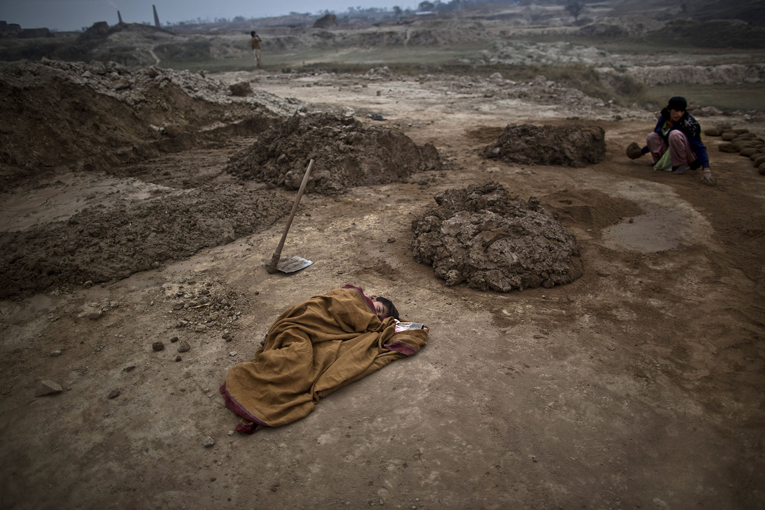 Mar. 3, 2014. 6-year-old Adil Shahid, suffering from a fever, sleeps on the ground wrapped with a shawl, next to the brick factory where his mother works in Mandra, near Rawalpindi, Pakistan.