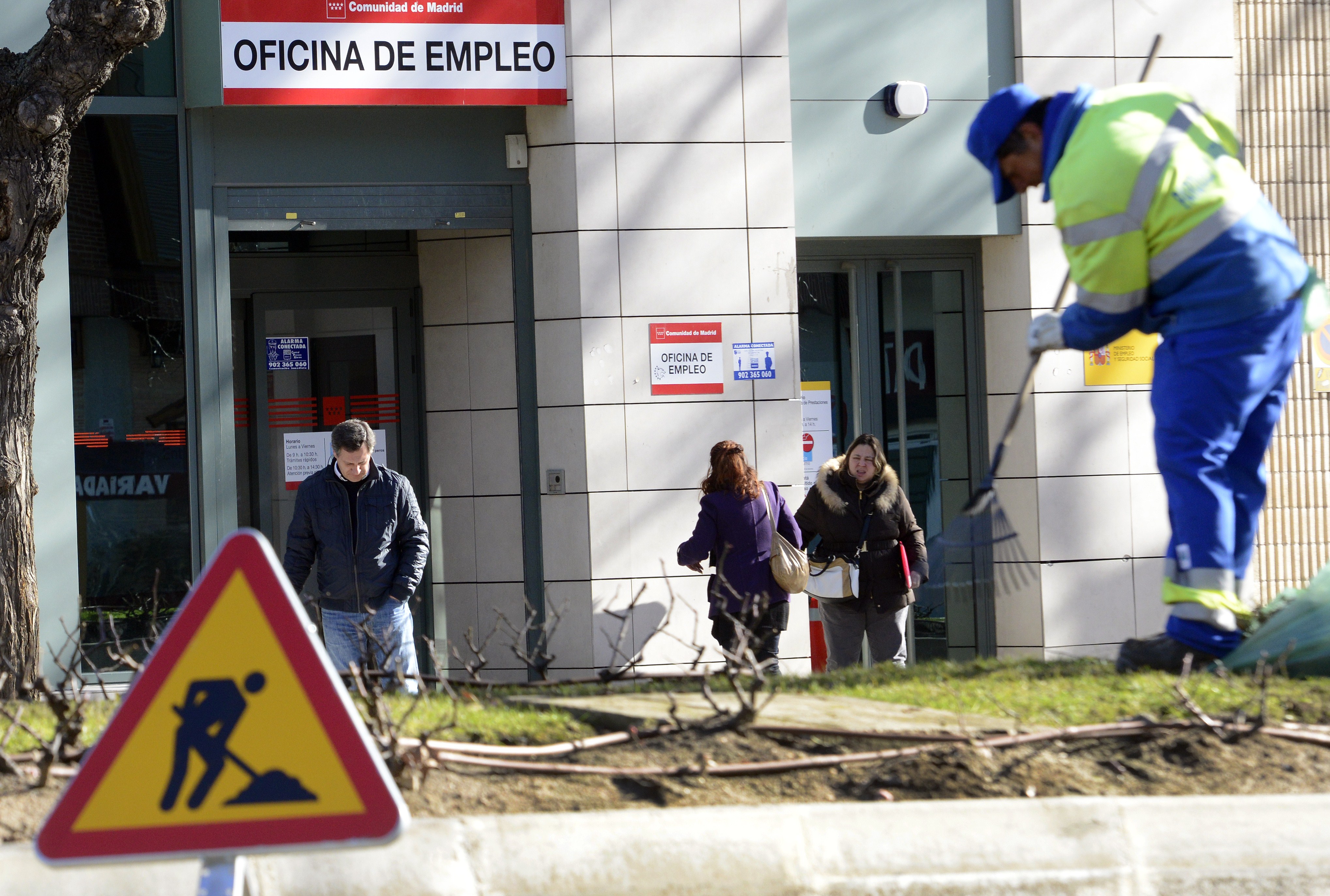 A municipal worker cleans the ground as people walk outside a government employment office in Madrid on January 23, 2014. (GERARD JULIEN / AFP / Getty Images)
