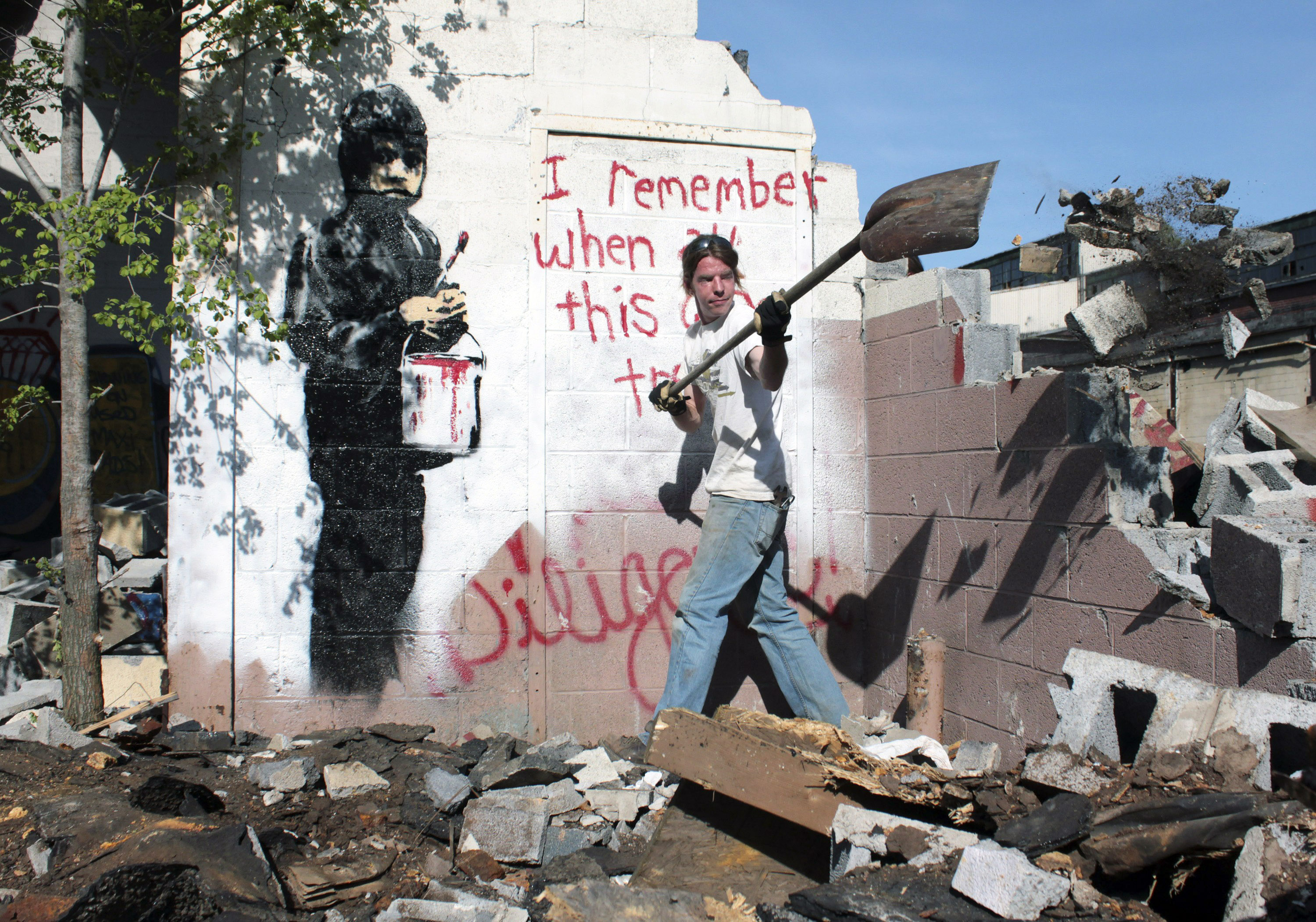 In this May 11, 2010 file photo Eric Froh,  conservator with 555 Nonprofit Gallery and Studios, clears the area around the stenciled artwork and message by British graffiti artist Banksy an abandoned car plant in Detroit before it was encased in a frame and taken to their gallery in Detroit. (Jerry S. Mendoza—AP)