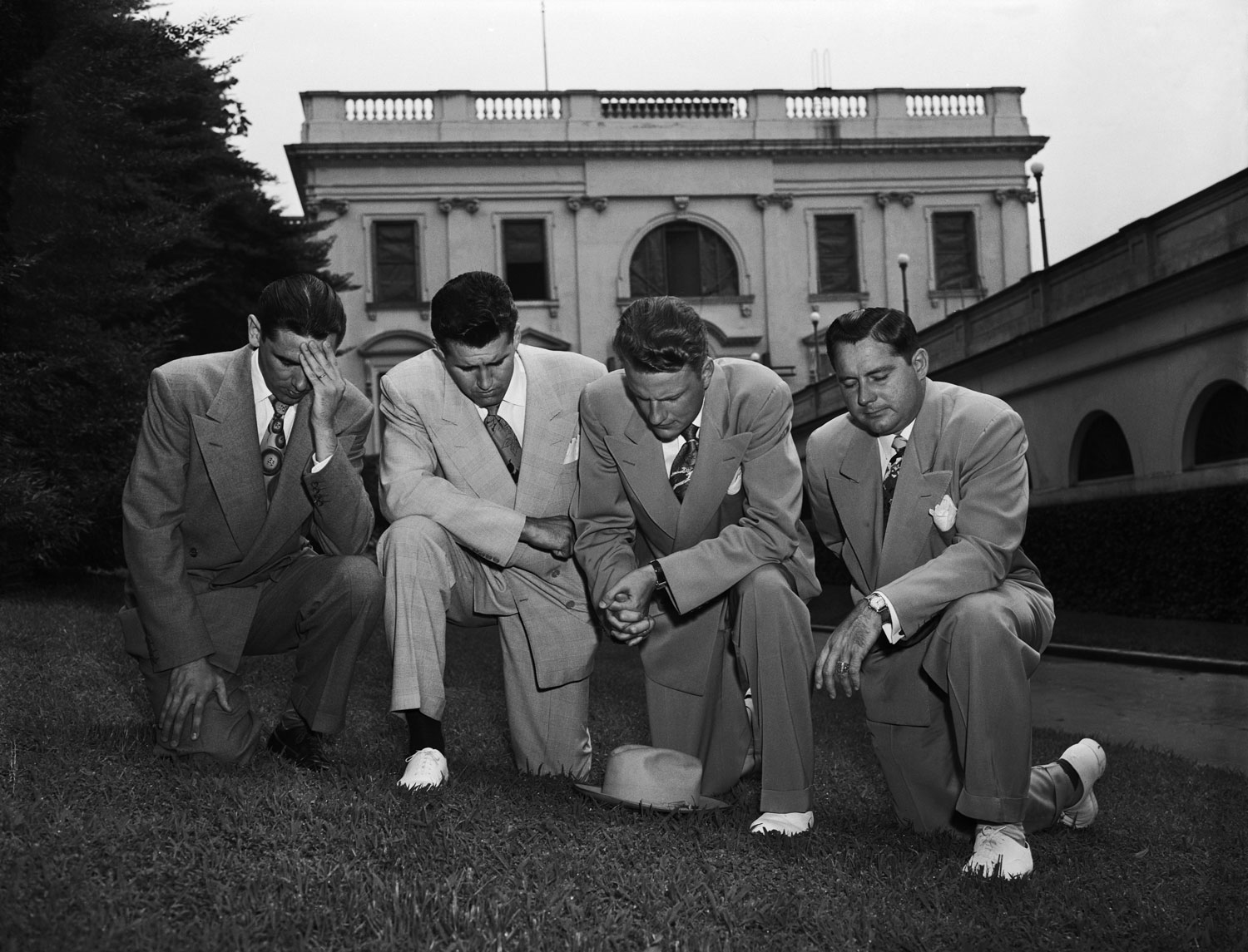 Graham, behind hat, kneels in prayer with fellow evangelists, from left to right, Jerry Beavan, Cliff Barrows and Grady Wilson after meeting with President Harry Truman to discuss the Korean War, July 14, 1950.