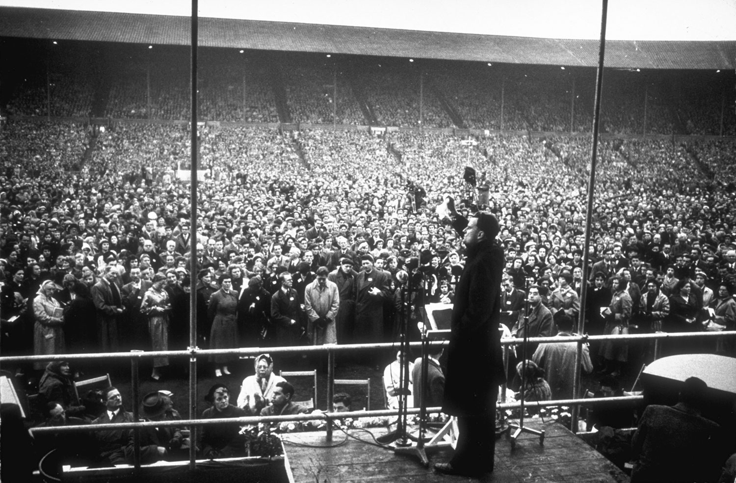 Graham waves a handkerchief while standing at a podium during a service in front of a crowd at Wembley Stadium.