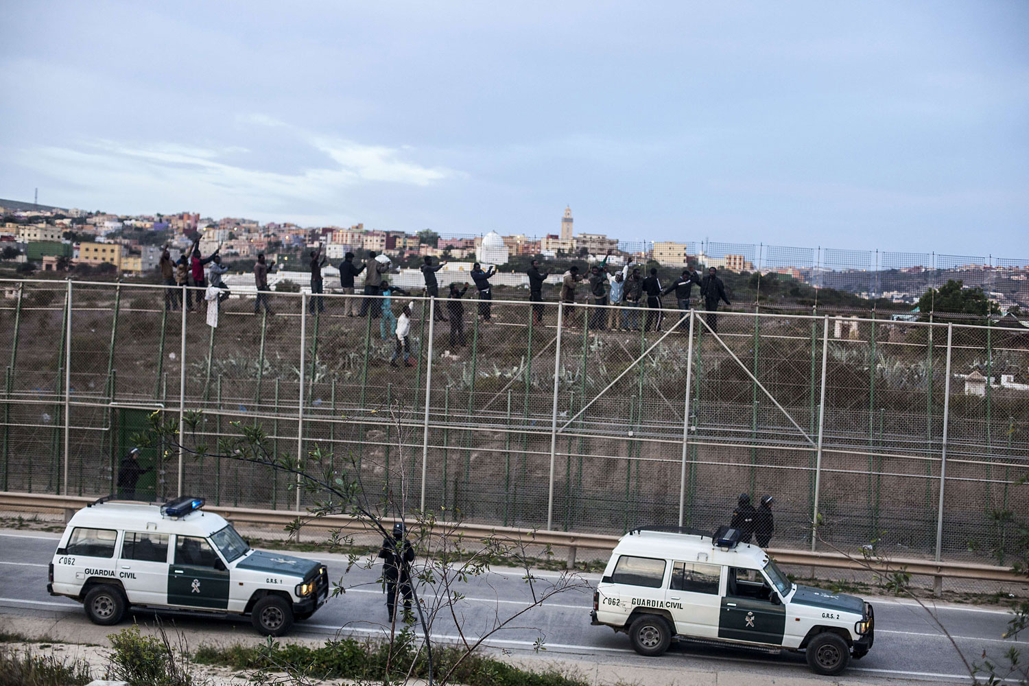 Spanish policemen watch would-be immigrants reacting between two fences near Beni Enza, into the north African Spanish enclave of Melilla on March 28, 2014.