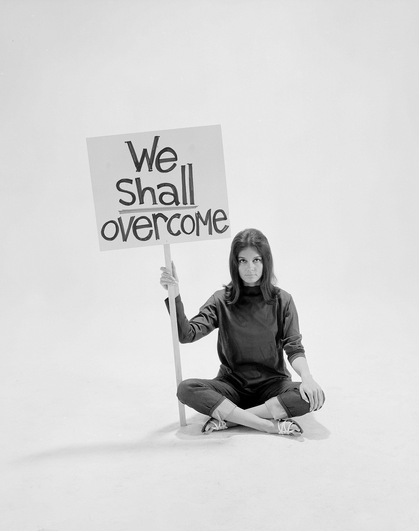 Writer Gloria Steinem sitting cross-legged on floor w. sign 