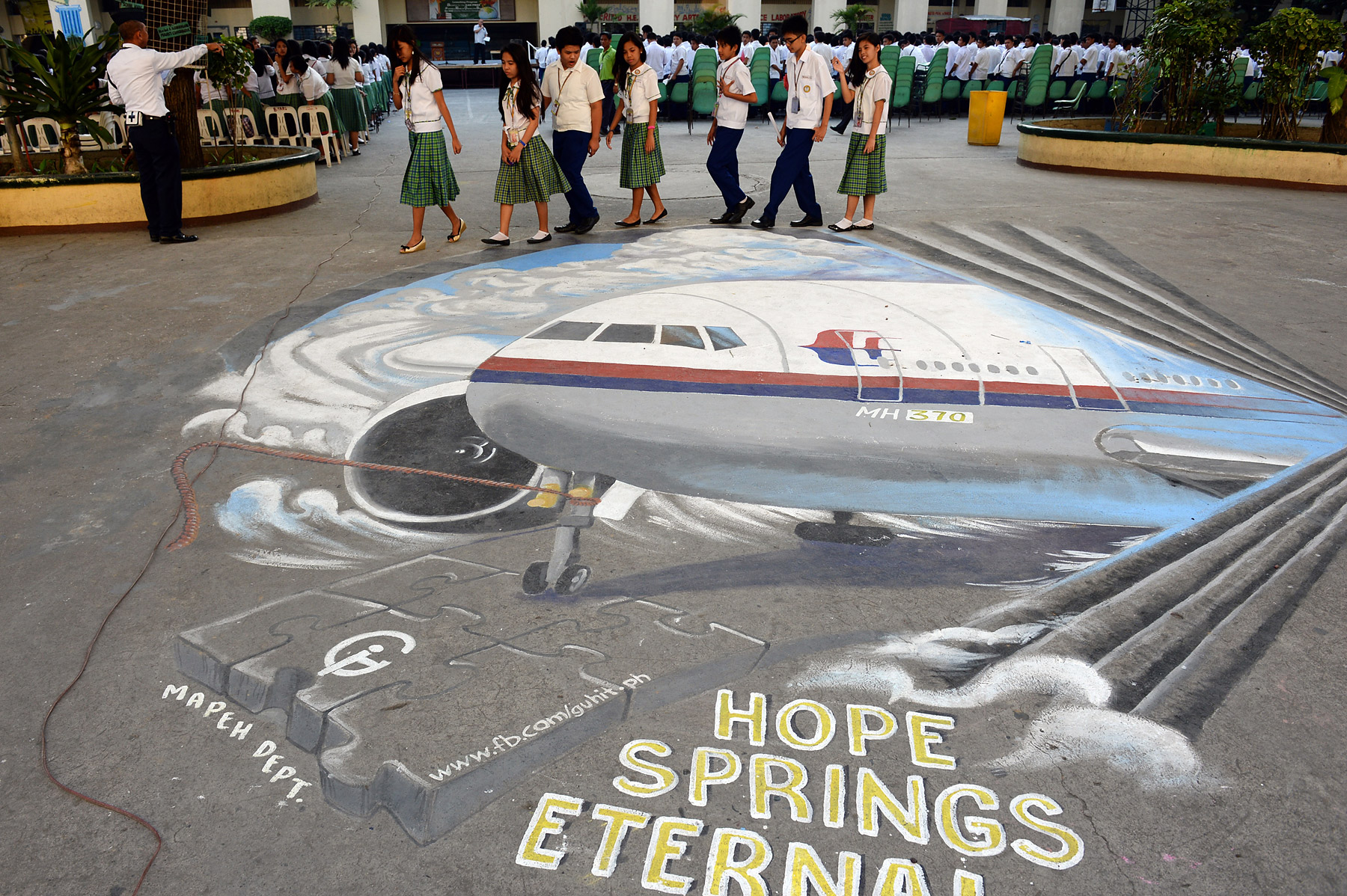 Students walk past a giant mural featuring the missing Malaysia Airlines Flight MH370, on the grounds of their school in Manila's financial district of Makati on March 18, 2014 (Ted Aljibe—AFP/Getty Images)