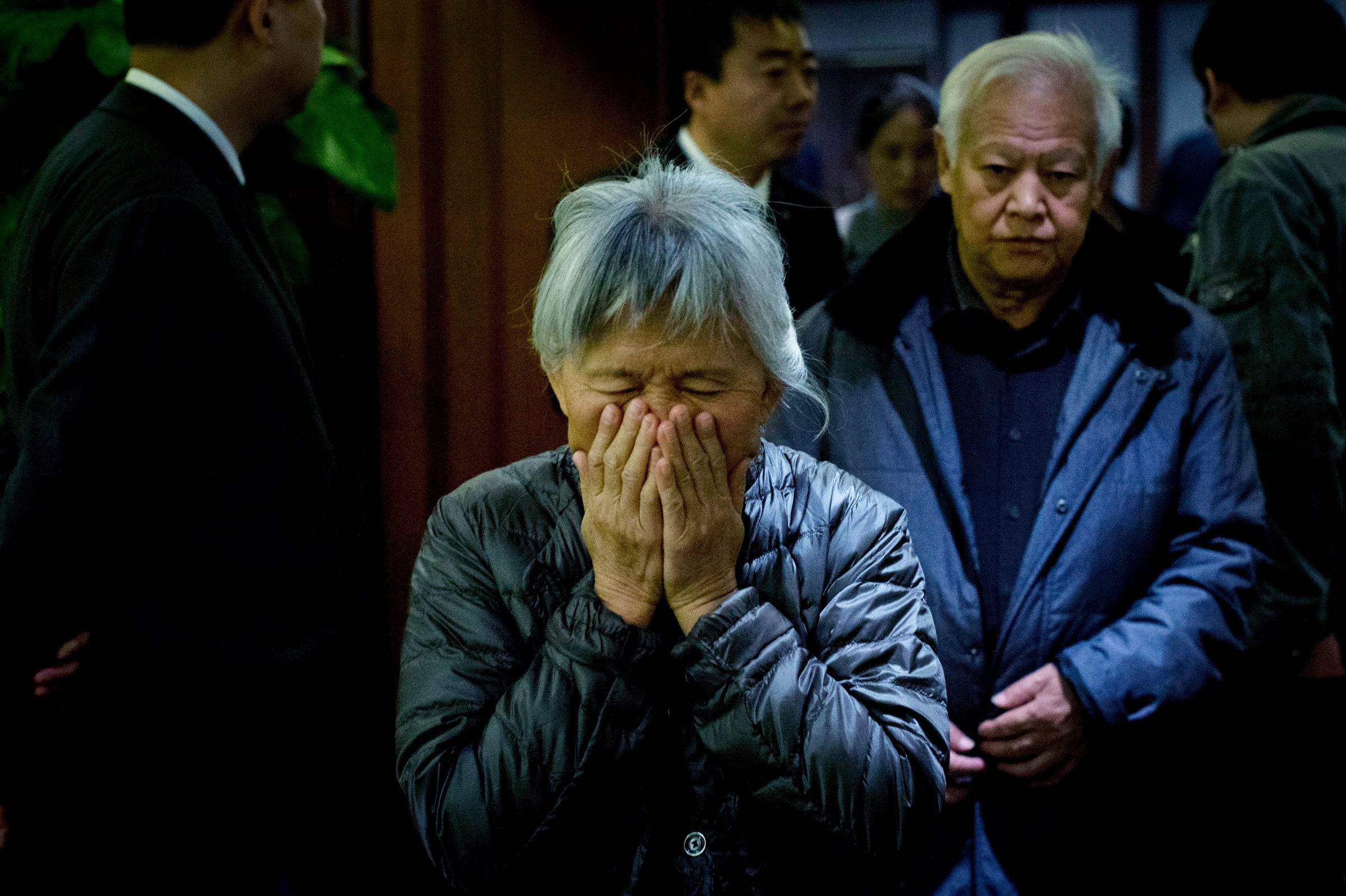 An elderly woman, one of the relatives of Chinese passengers aboard missing Malaysia Airlines Flight MH370, covers her face out of frustration as she leaves a hotel ballroom after a daily briefing meeting with managers of Malaysia Airlines in Beijing, on March 19, 2014.