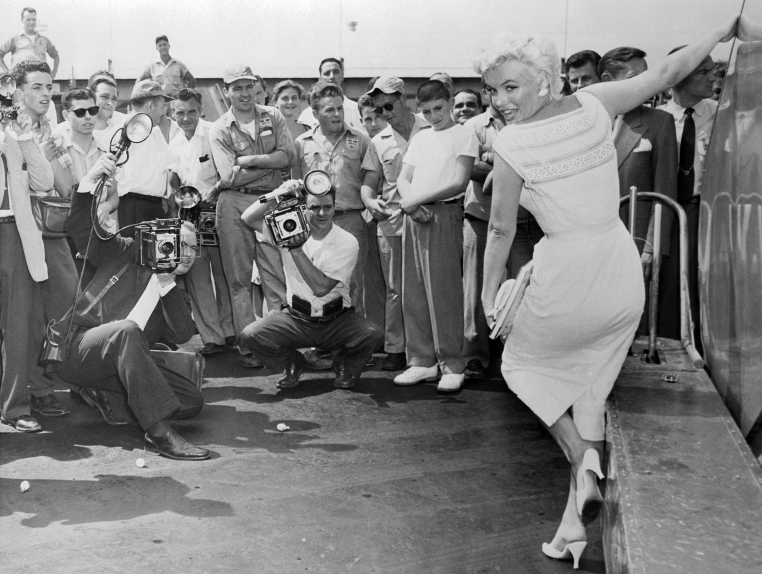 Carrying a book on the life of Abraham Lincoln, Marilyn Monroe tears herself away form it long enough to pose for photographers at Idlewild Airport just before she took off for Bement, Illinois.