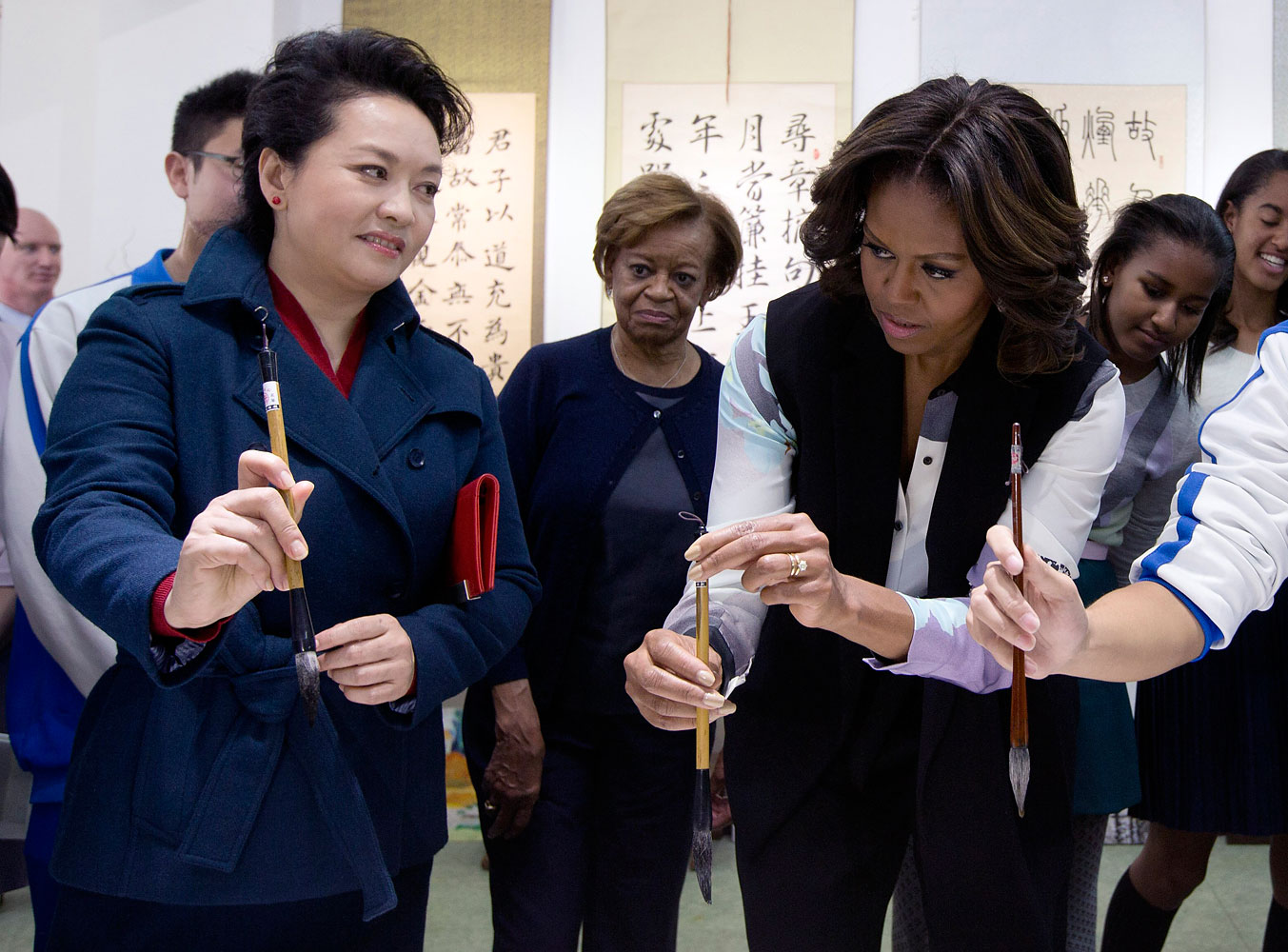 Peng Liyuan, wife of Chinese President Xi Jinping shows U.S. first lady Michelle Obama how to hold a writing brush as they visit a Chinese traditional calligraphy class at the Beijing Normal School, a school that prepares students to go abroad in Beijing, March 21, 2014.